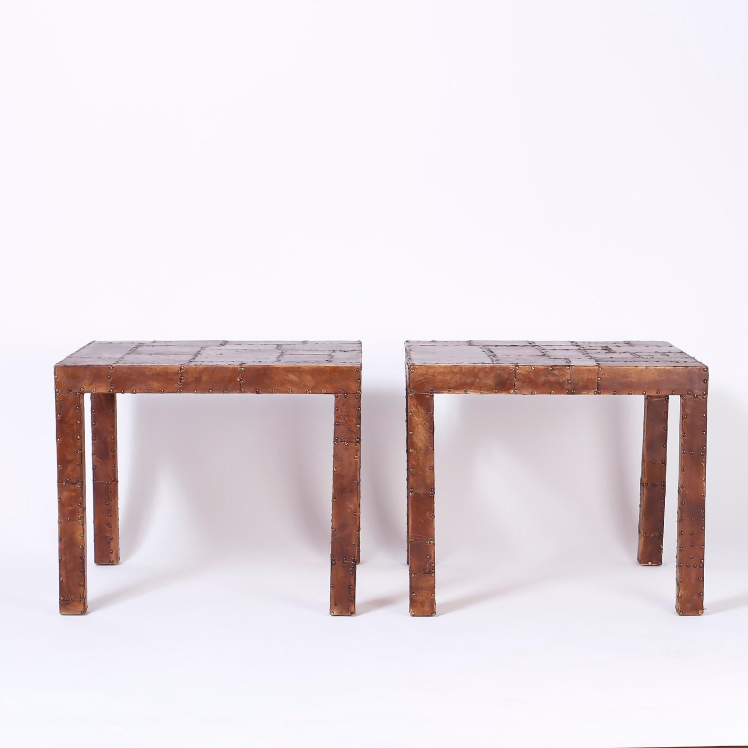 Swank pair of midcentury end tables with a Classic Parson's form entirely clad in patches of brown leather with brass tacks giving these tables an unusual warm industrial ambiance.