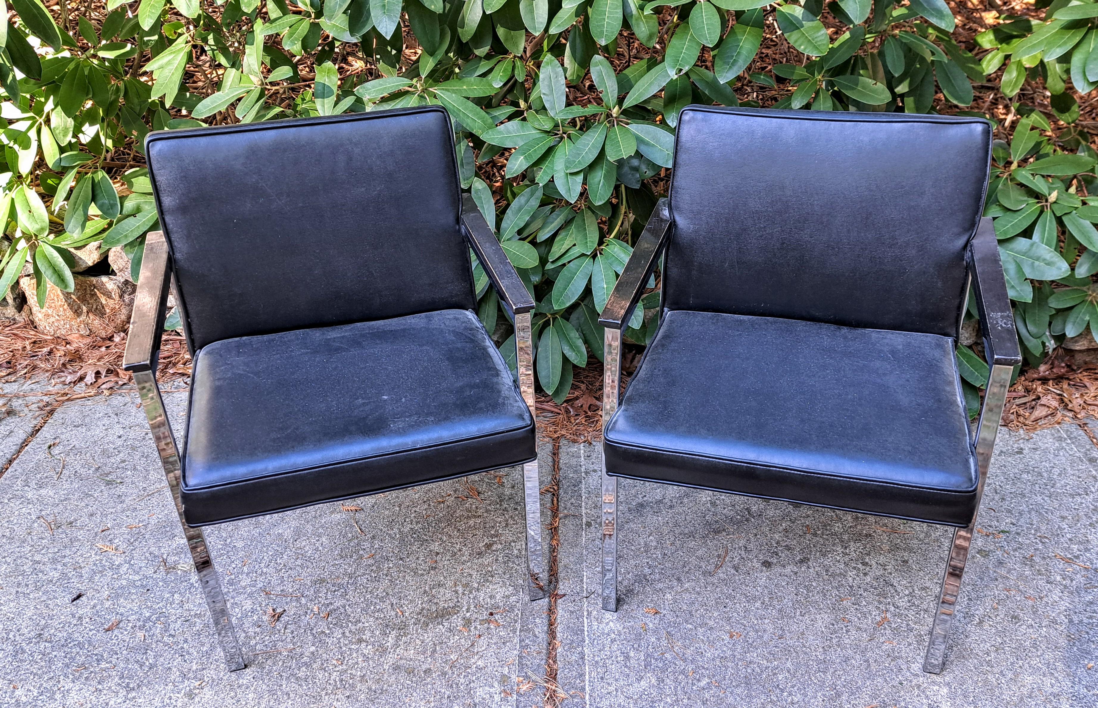 Coppia di poltrone in vinile nero e cromo. Le sedie hanno braccioli a paletta in legno e una spessa barra di supporto laterale cromata. 