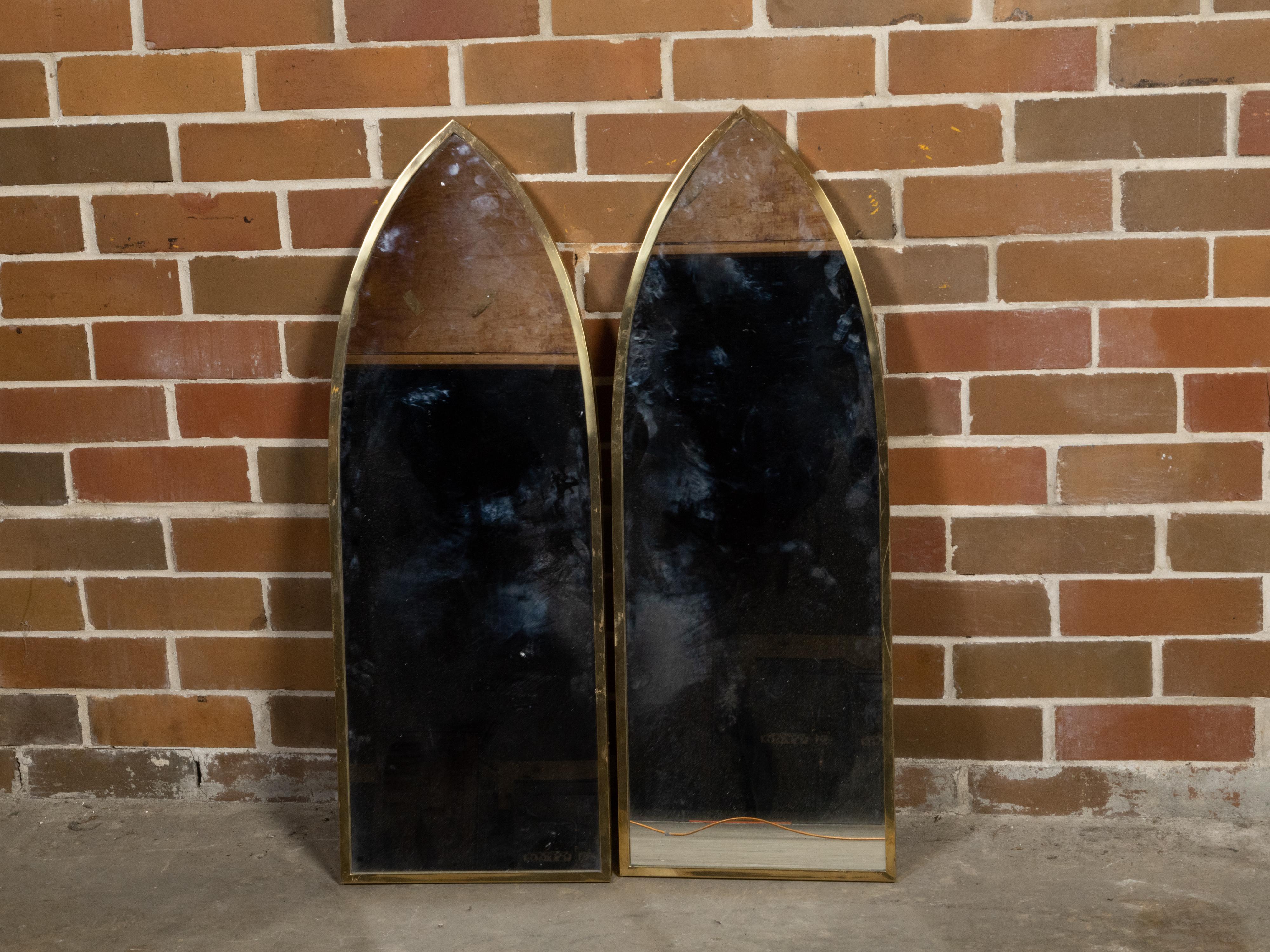 A pair of European vintage Neo Gothic style brass wall mirrors from the mid 20th century, with pointed arch silhouettes. Created during the Midcentury period, this pair of vintage European mirrors draws our attention with their Neo Gothic lines