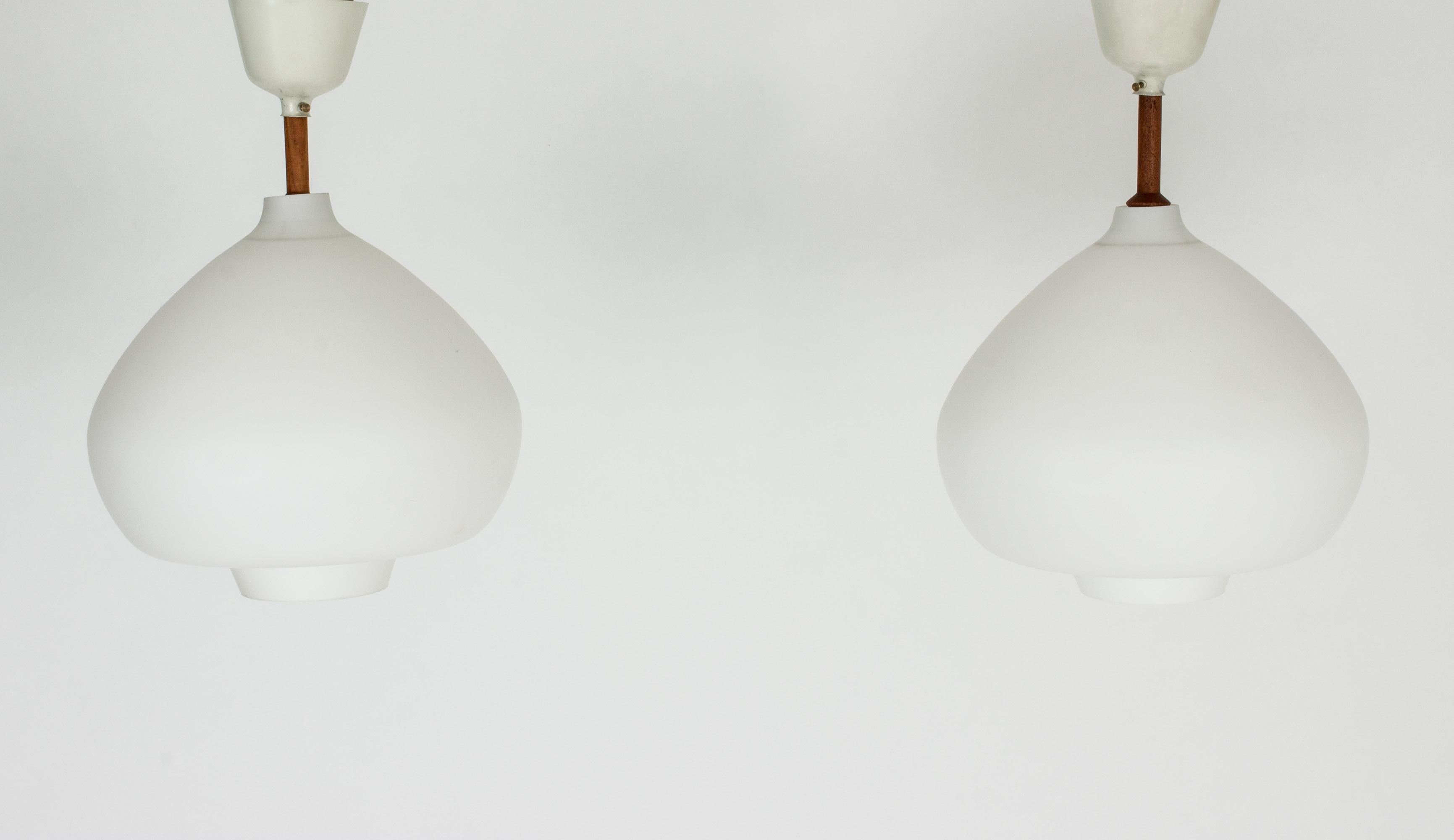 Pair of voluptuous opaline glass ceiling lamps by Hans-Agne Jakobsson, designed to sit close to the ceiling, suspended from a teak pole. Lacquered metal cups.