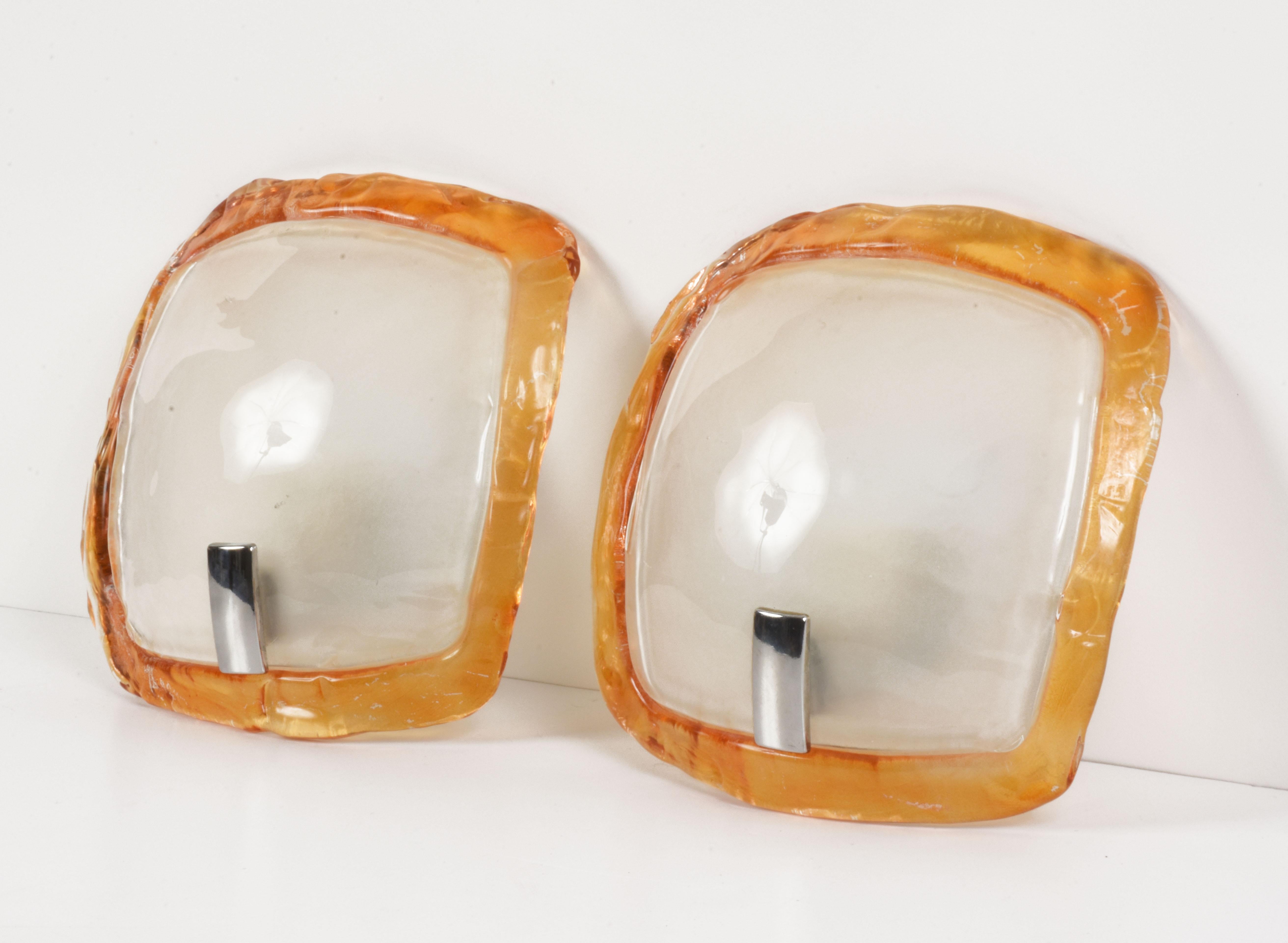 Pair of orange and crystal Murano glass sconces with iron finishes. Produced in Italy during 1980s.

They consist of two parts, an orange and crystal Murano glass element resting on a metal base. Both elements influence the refraction of light,