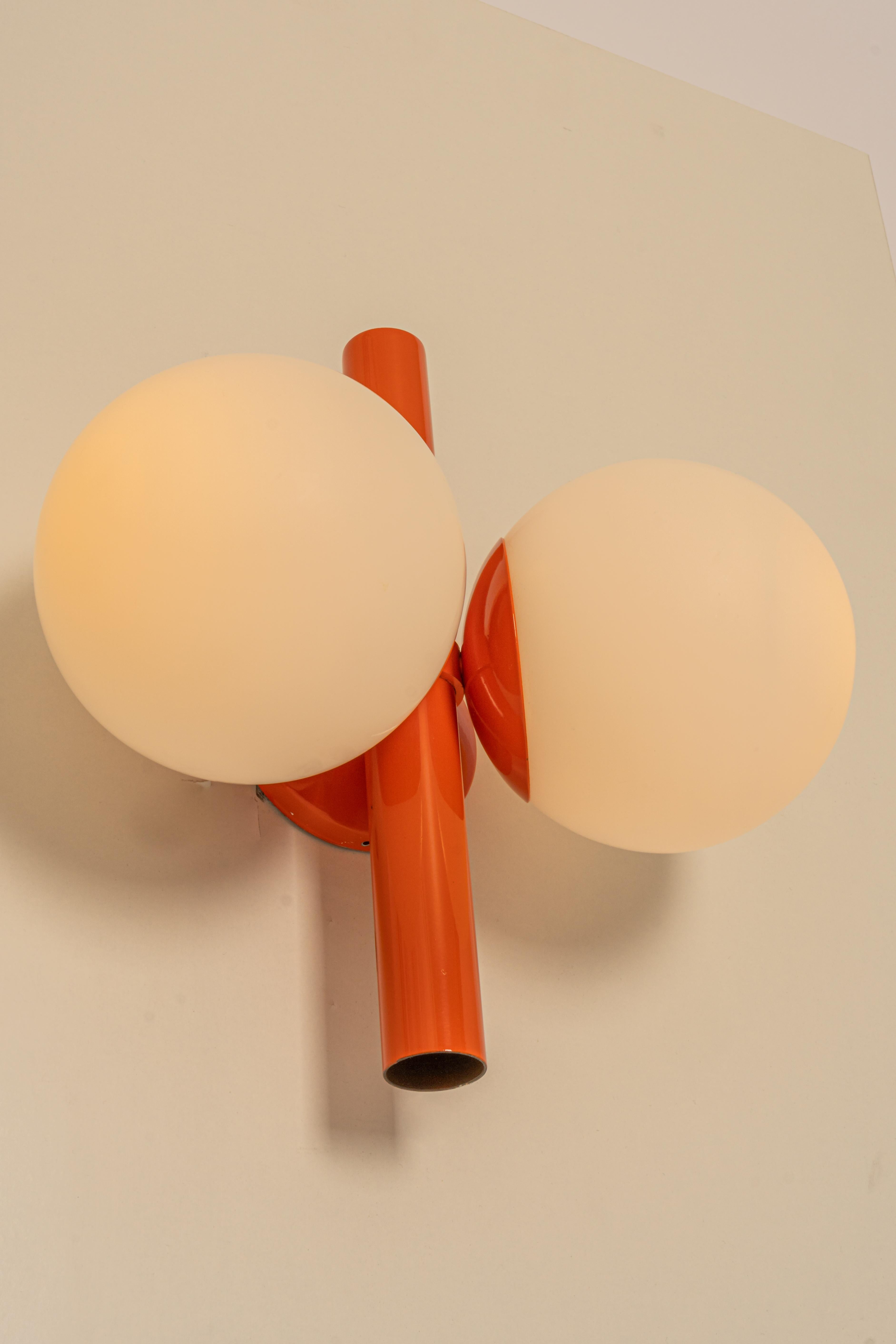1 of 2 mid-century vintage wall lights in orange color made by Kaiser Leuchten, Germany with 2 opal glass balls.
High quality and in very good condition. Cleaned, well-wired, and ready to use. 

The fixture requires 2 x E14 small bulbs with 40W