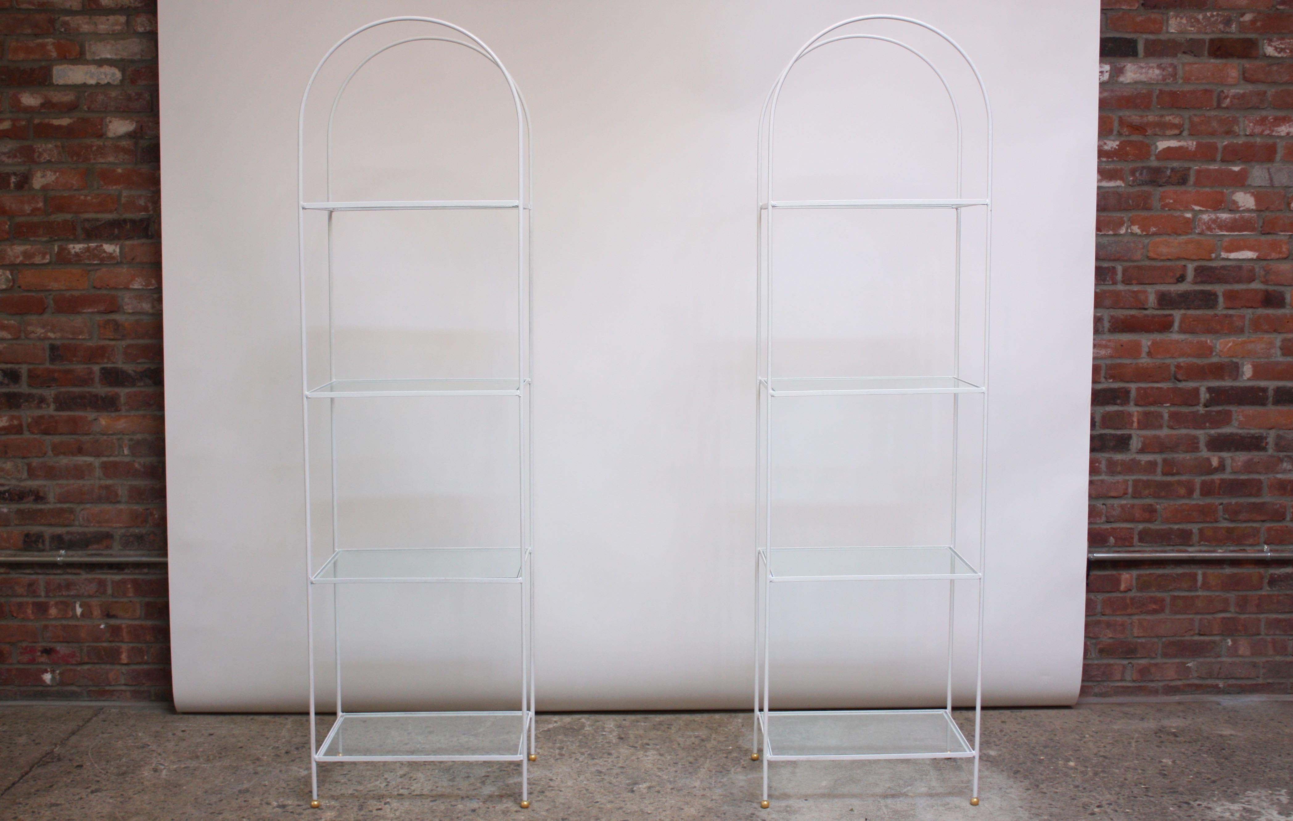 Pair of 1960s arched shelving units / book shelves / etageres composed of white wrought iron frames with inset glass shelves (four / unit). 'Ball' feet have been freshly painted gold; white paint is original and is in good, vintage condition with