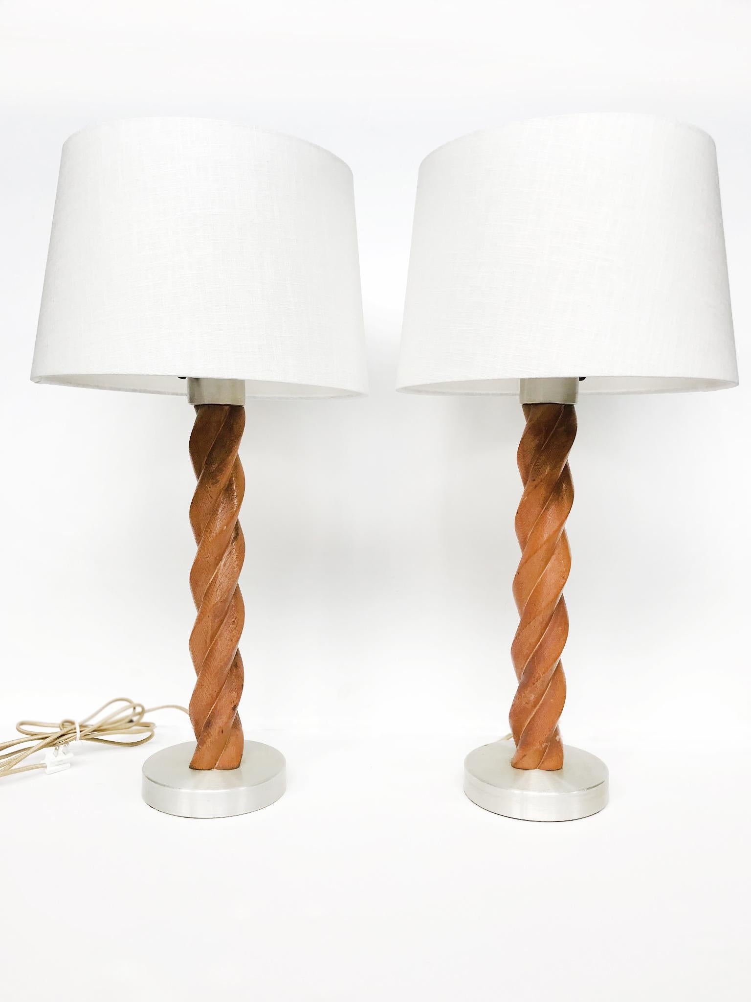 An elegant pair of table lamps attributed to the American designer Russel Wright. The lamps are comprised of a sculptural, twisting stem carved from oak and a circular aluminum base and insulate sleeve. The wood is richly stained in a warm honey