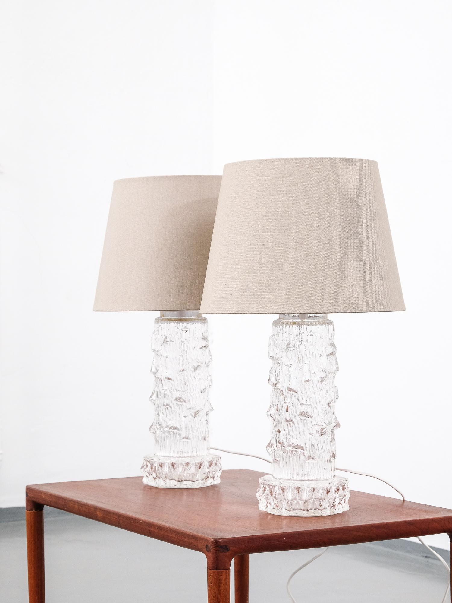 Great pair of midcentury Scandinavian table lamps. The clear glass leg has ice-like pattern. Unknown designer.

Measures: Height with shade 55 cm.