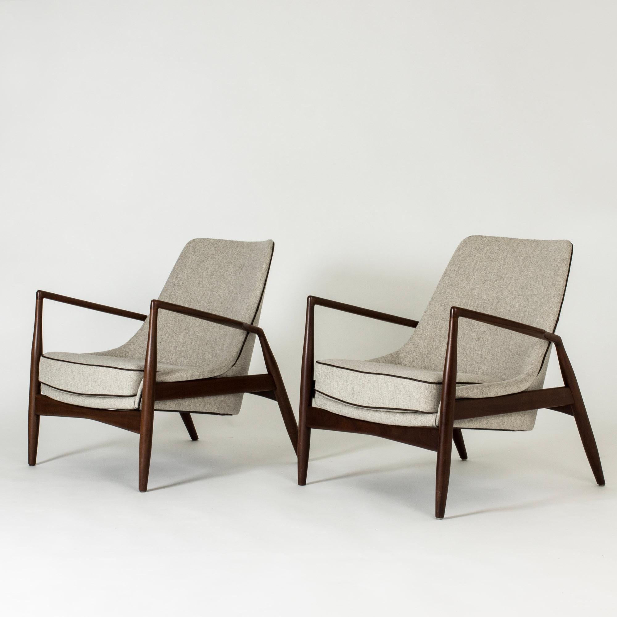 Pair of amazing “Seal” lounge chairs by Ib Kofod Larsen, made with teak frames. Light grey upholstery with dark brown leather piping. Great silhouettes and materials, sculpted winglike armrests.