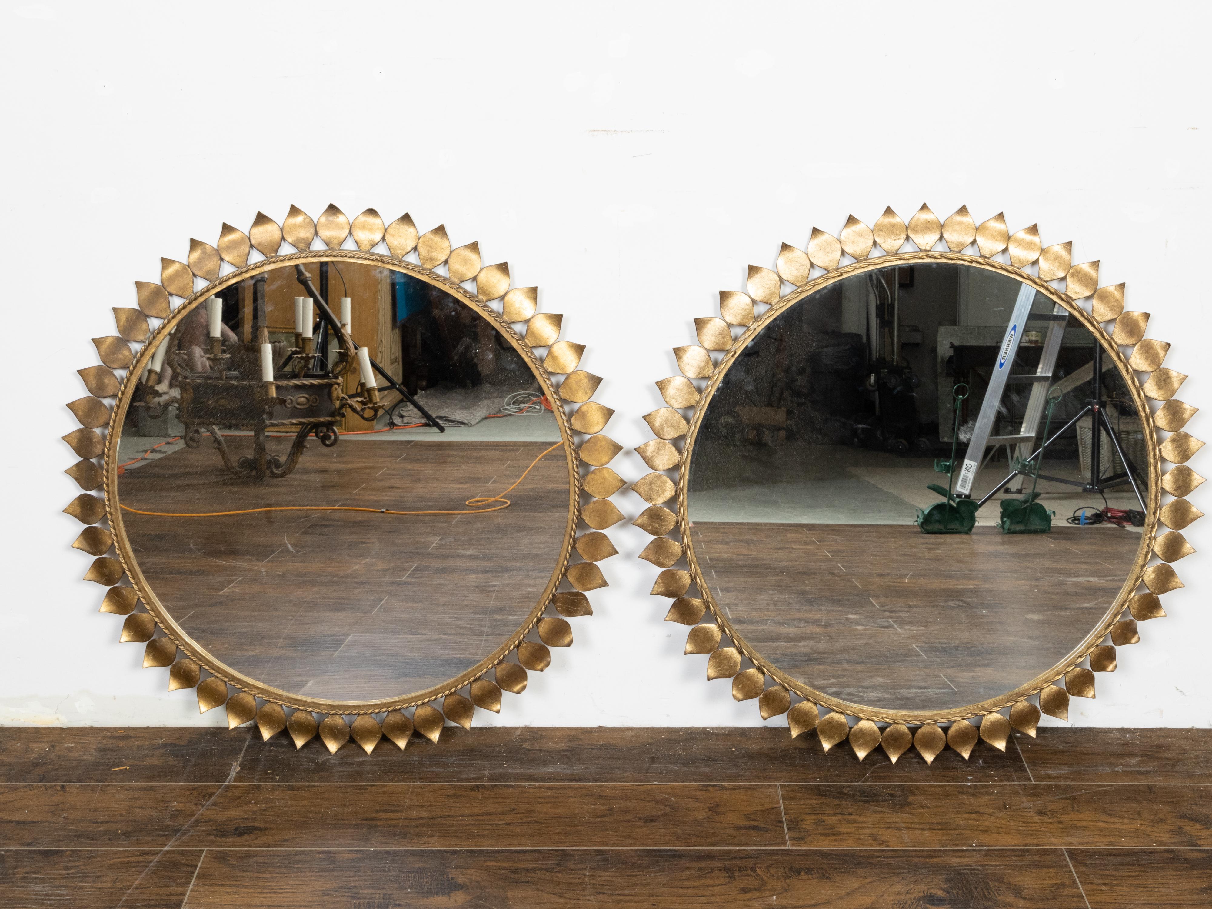 A pair of Spanish vintage gilt metal mirrors from the mid 20th century, with circular frames, twisted ropes and foliage motifs. Created in Spain during the midcentury period, each of this pair of wall mirrors features a circular gilt metal frame