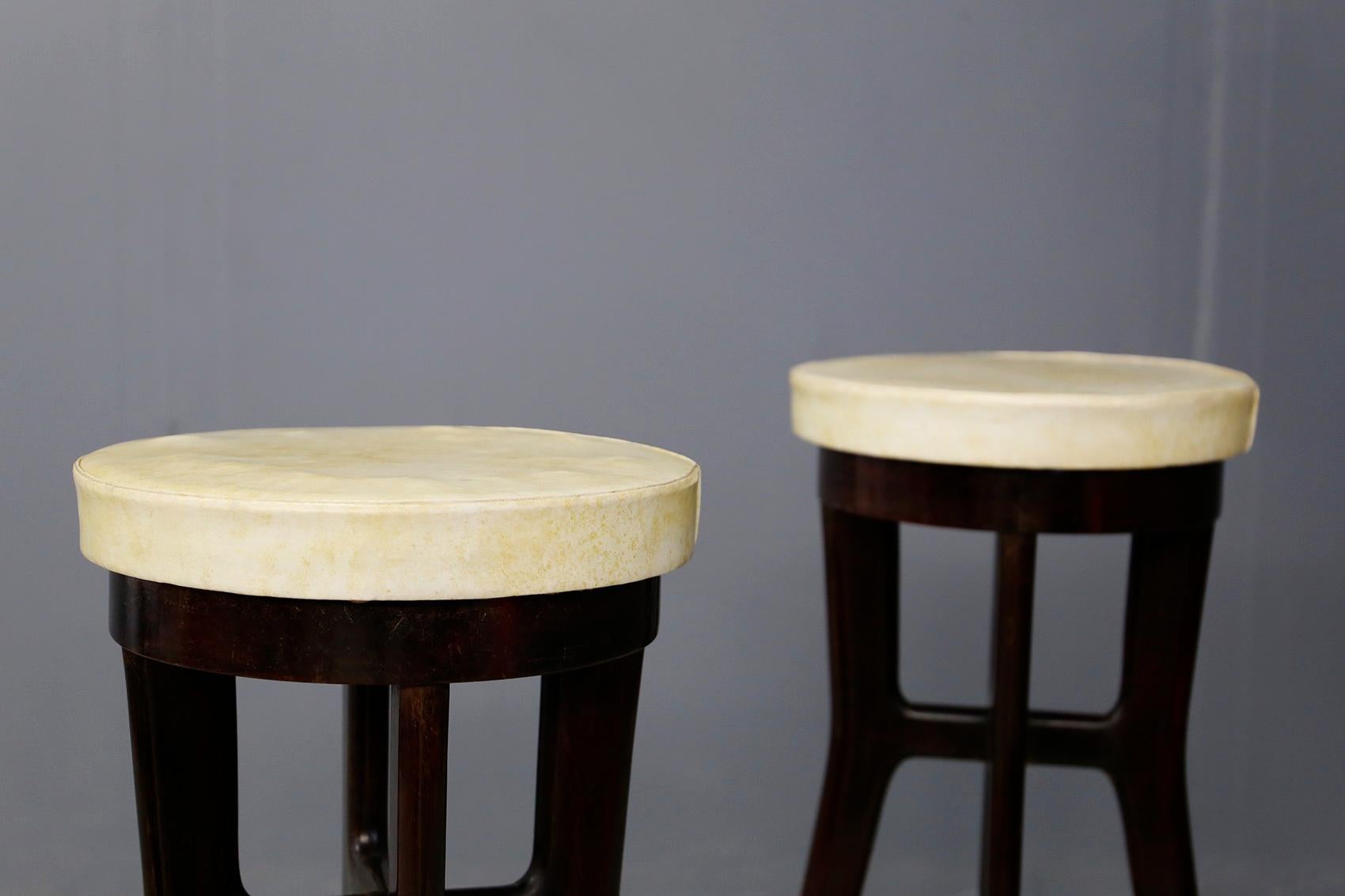 Pair of elegant high stools attributed to Osvaldo Borsani from 1950. The stools are made of walnut wood with 4 conical feet. The seat is covered in cream-colored semi leather. To improve the half-leg seat we find a brass tubular semicircle that