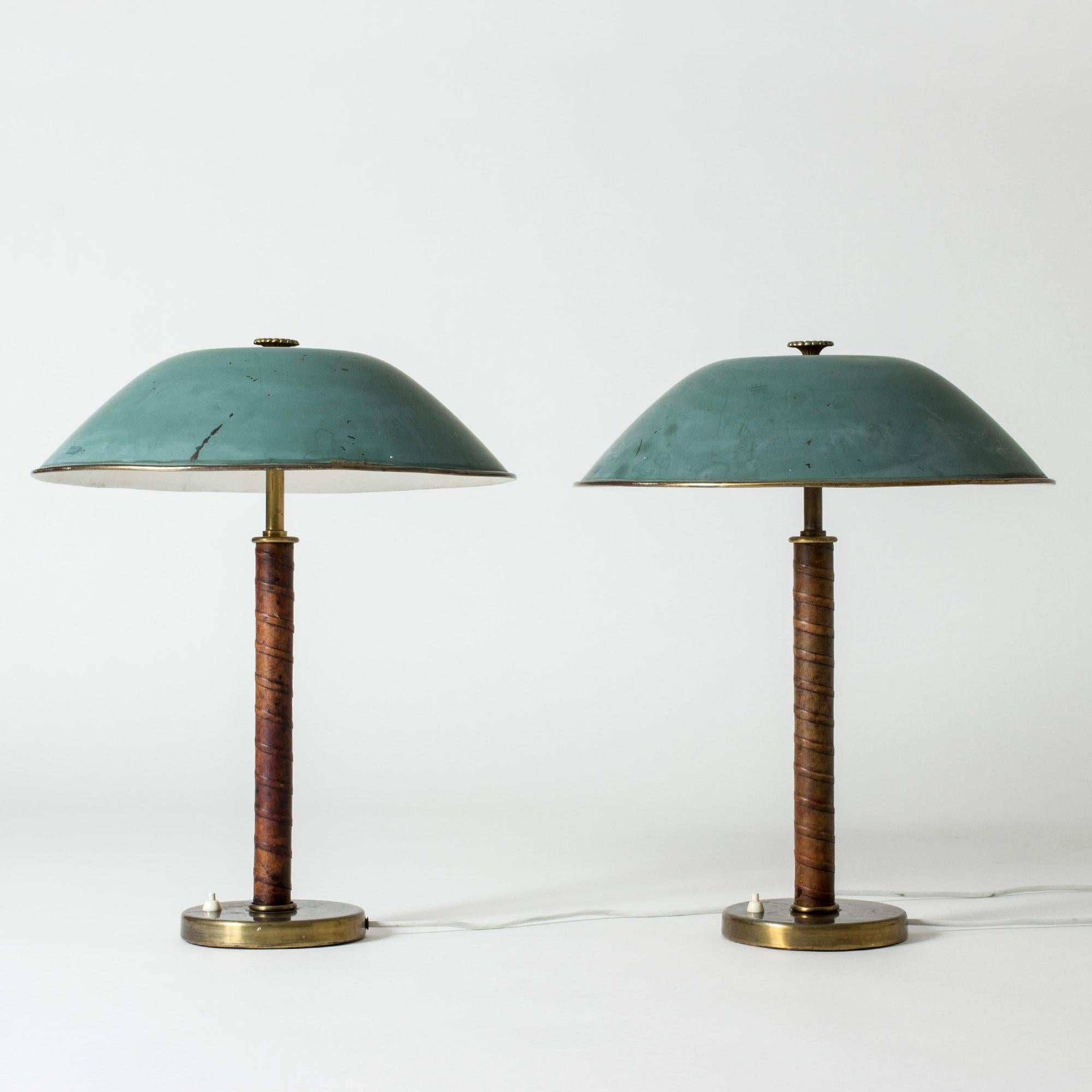 Pair of beautiful brass table lamps from NK, with green lacquered shades and leather wound stems. Decorative flower knobs on top. Original condition with wear on the shades.