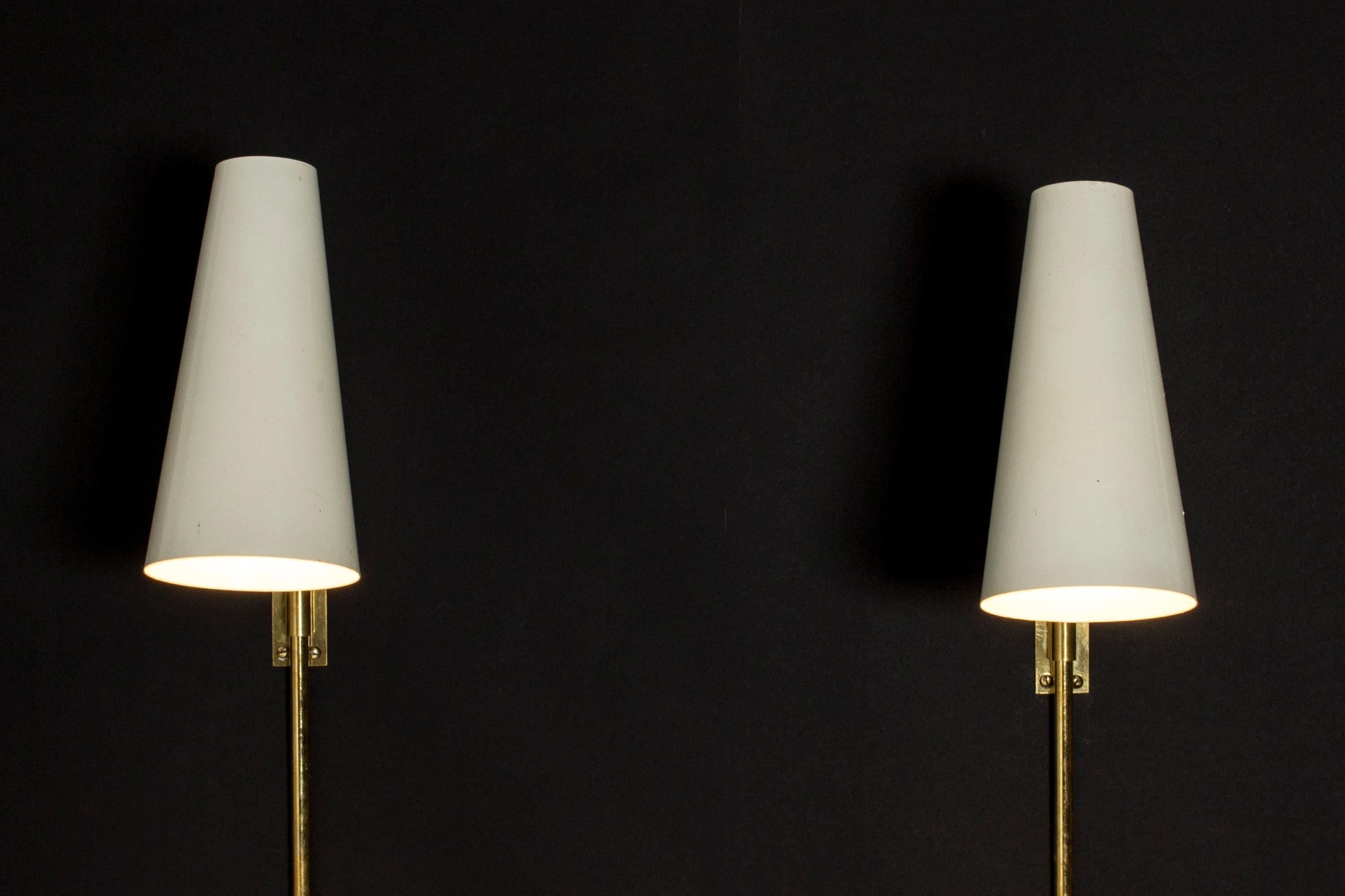 Pair of elegant, minimalist wall lamps by Paavo Tynell. White lacquered metal shades on brass handles, neat brass screw mechanisms for adjusting the positions.

Size: Height adjustable, 34 cm-38 cm, width 9.5 cm, depth 23.5 cm.