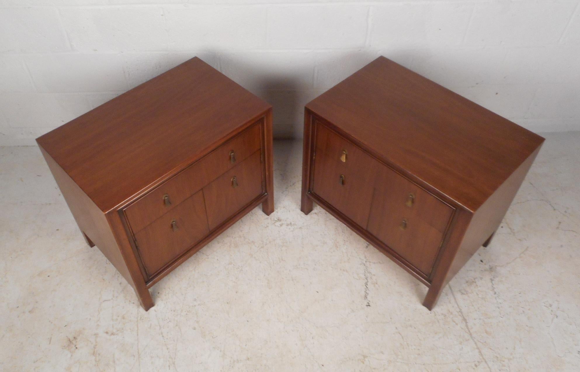 This beautiful pair of Mid-Century Modern nightstands boast unique hanging brass pulls and a dark vintage walnut finish. A stylish design that provides ample space for storage within its hefty drawer and large compartment. Quality craftsmanship with