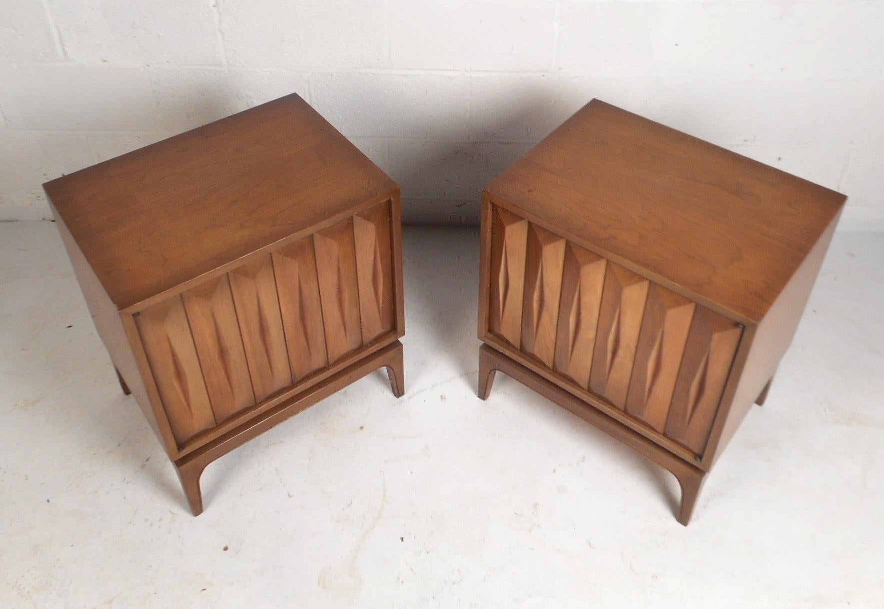 These beautiful Mid-Century Modern walnut end tables feature swinging cabinet doors with a three dimensional sculpted pattern on the front. This stylish pair offers plenty of room for storage within its large compartment with a shelf. The legs of