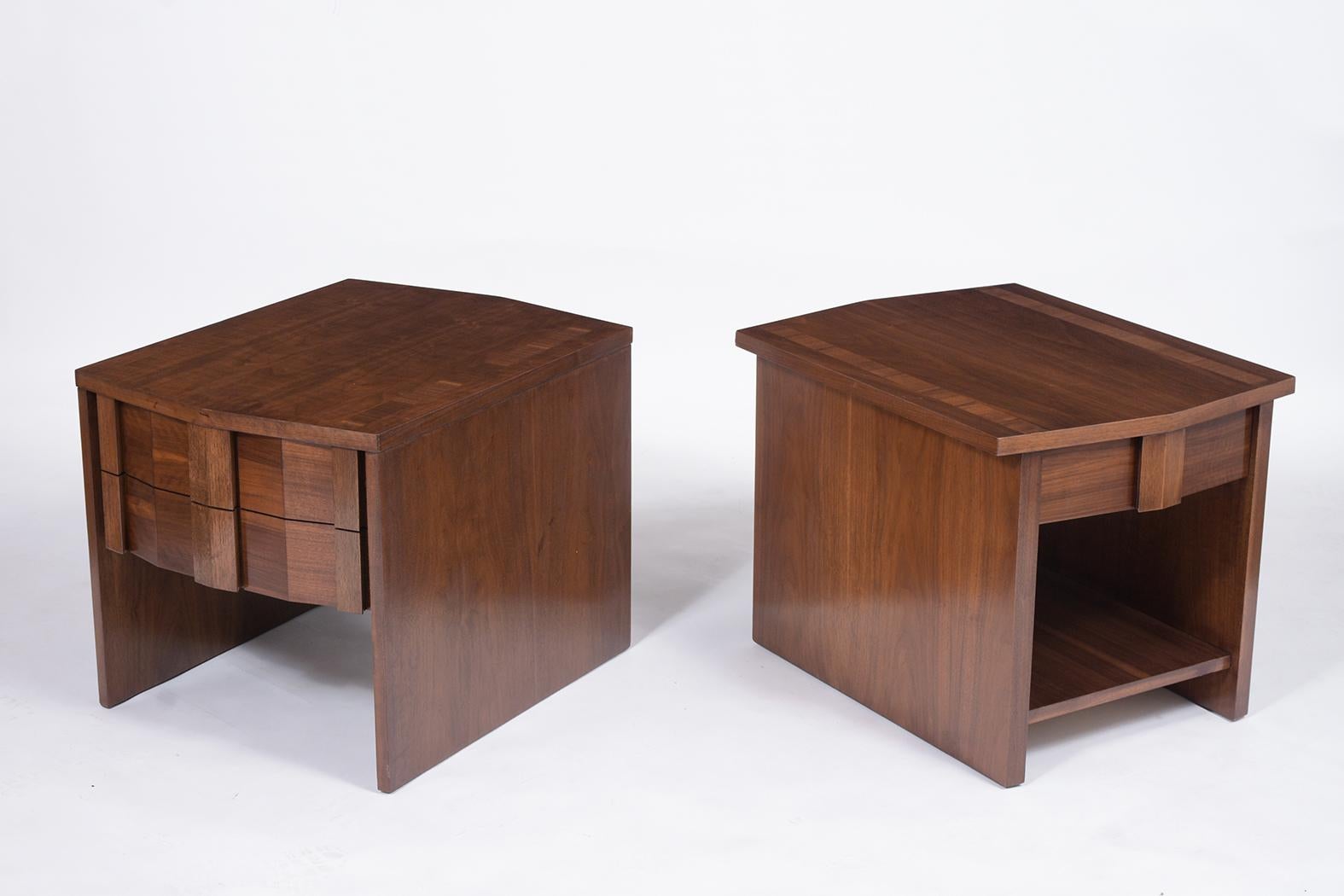 A sleek pair of midcentury nightstands that are professionally restored are made out of walnut wood and are newly stained in a walnut color with a lacquered finish. They feature a flat top diamond design with a double and single door and open shelf