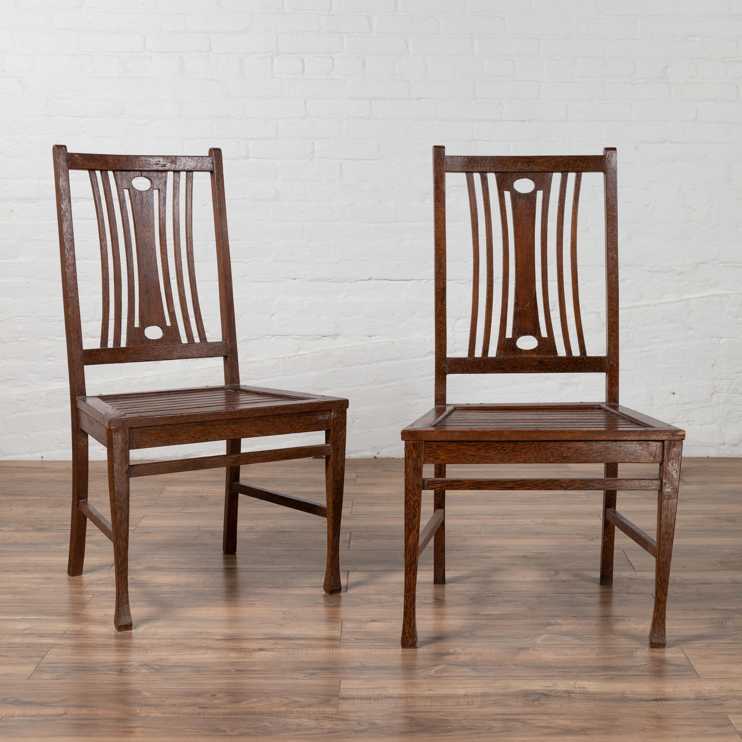A pair of vintage Indonesian wooden side chairs from the mid-20th century, with pierced splats. We currently have two or more pairs available, priced and sold per pair. Born in Indonesia during the midcentury period, each of this pair of side chairs