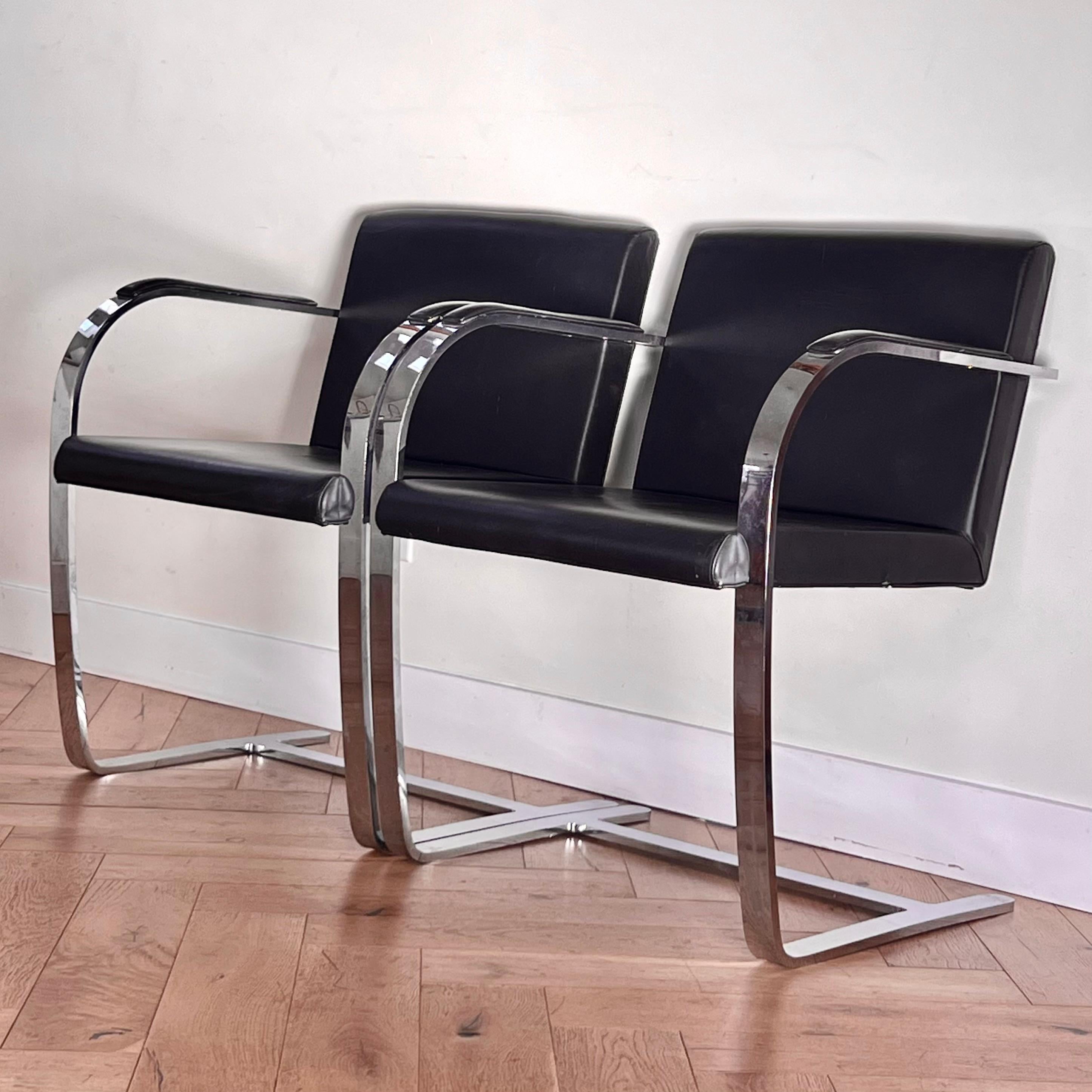 A pair of Brno flat arm chairs in chrome and black leather, circa 1970s. Designed by Mies van der Rohe in 1930, these are authorized reproductions made according to the original specifications by Palazzetti Italy. Some signs of age, including