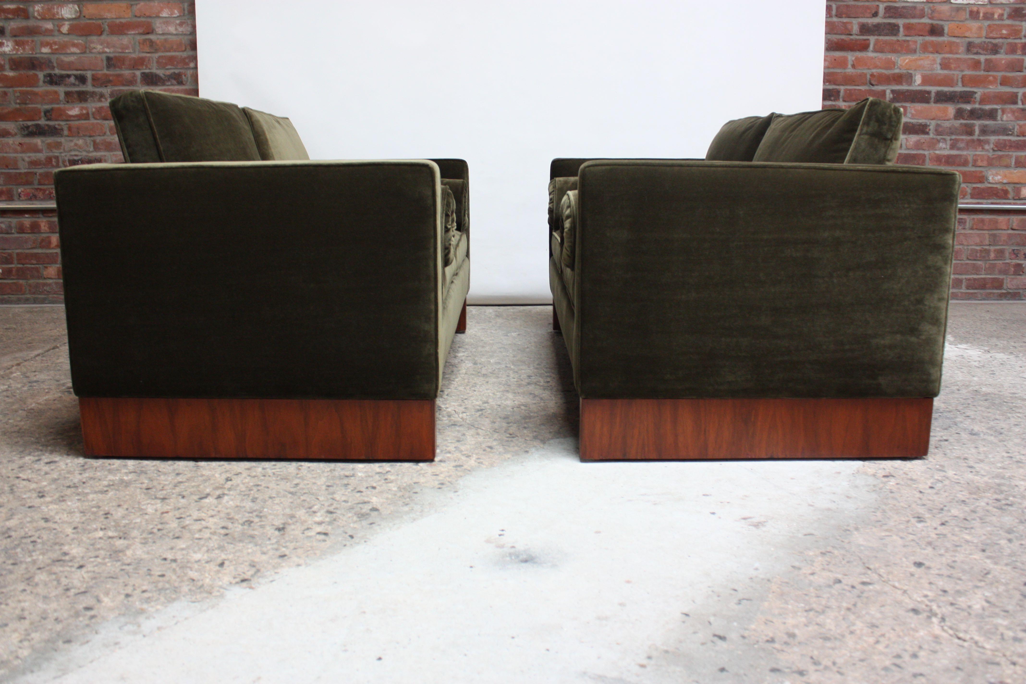 Rare pair of Ludwig Mies van der Rohe for Knoll International settees (circa 1960) composed of dual teak plinth bases which support a newly reupholstered olive green velvet frame with corresponding bolsters. Hand-sewed details / tufting executed to