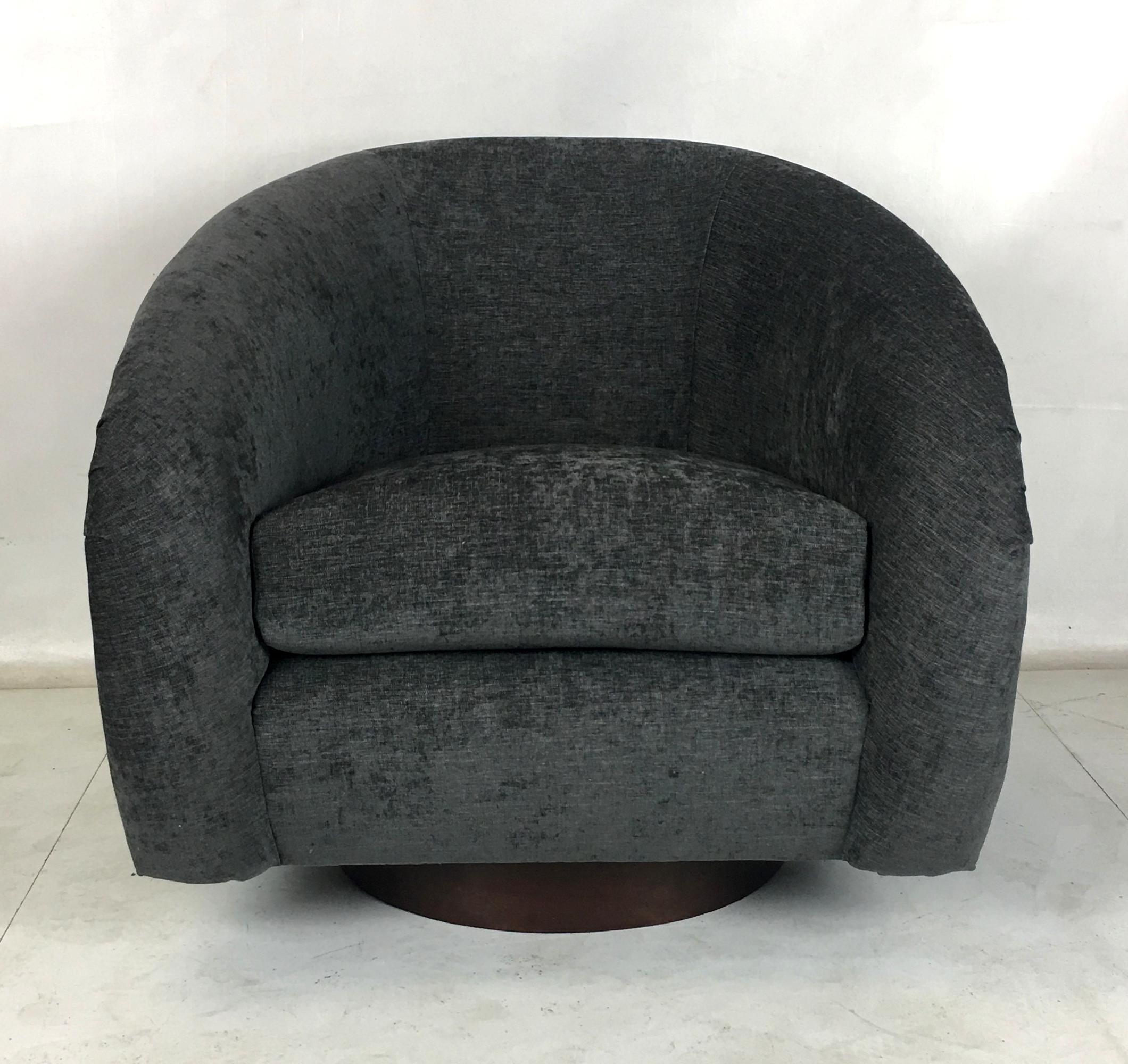 Pair of Milo Baughman roll arm swivel chairs raised on walnut veneer circular bases. The pair have been freshly upholstered in charcoal gray tweed upholstery. The bases have been refinished with new swivel plates. These chairs are luxuriously
