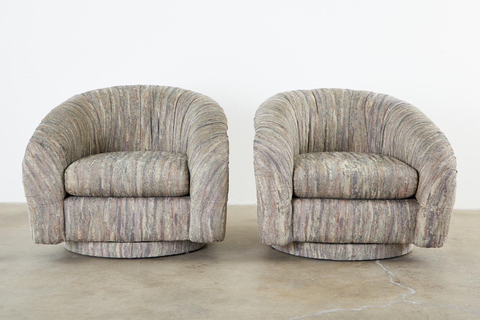 Iconic pair of swivel lounge chairs or club chairs in the Mid-Century Modern style after Milo Baughman. Featuring a round barrel form upholstered with a late 1970s or 1980s style of fabric. Very presentable and comfortable with minimal wear in good