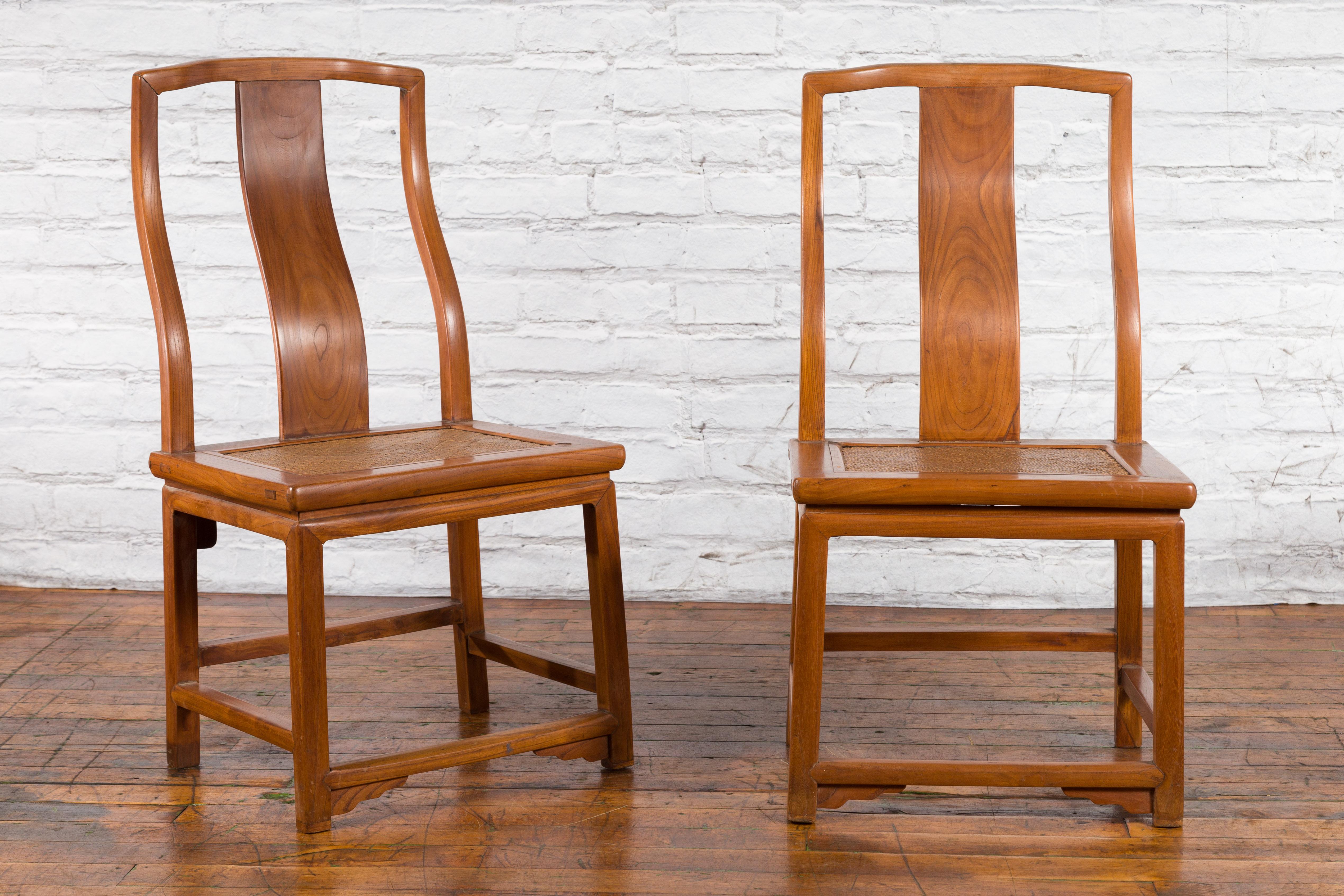 A pair of Chinese Ming dynasty style yoke back side chairs from the early 20th century with woven rattan seats, curving back splats and natural wood patina. Created in China during the early years of the 20th century, each of this pair of side