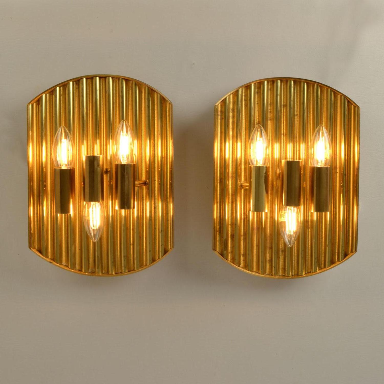 Coppia di applique minimaliste in ottone in perfetto equilibrio geometrico, ognuna delle quali sostiene tre lampade verso l'alto e verso il basso. La superficie è realizzata in lamiera d'ottone ondulata e rifinita con un'alternanza di linee