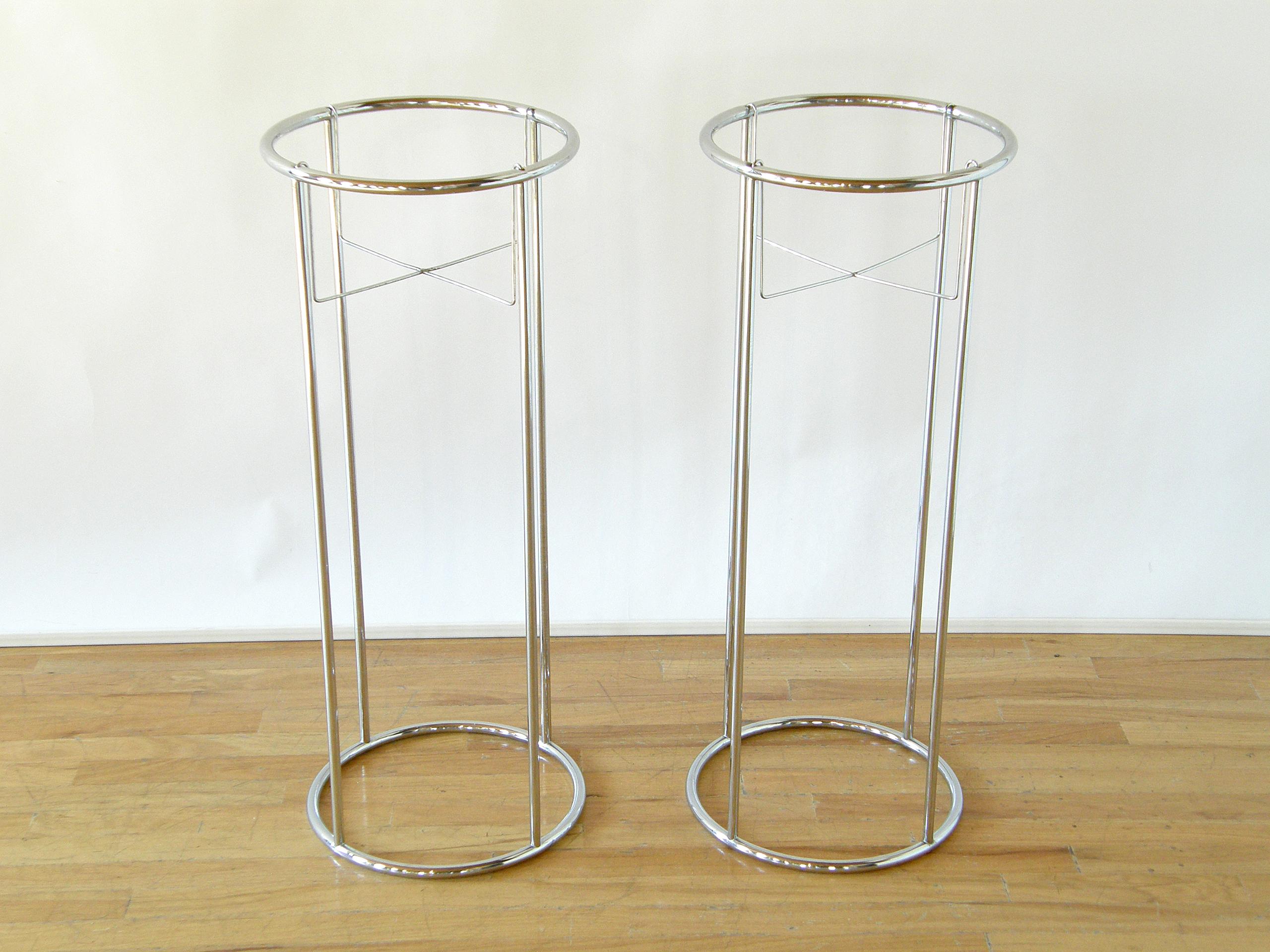This pair of chrome plant stands has an elegant, Minimalist style. The slender, tubular chrome forms a skeletal, columnar framework. From that hangs a wire cradle that holds your potted plant aloft, like a pedestal for a plant. The chrome reflects