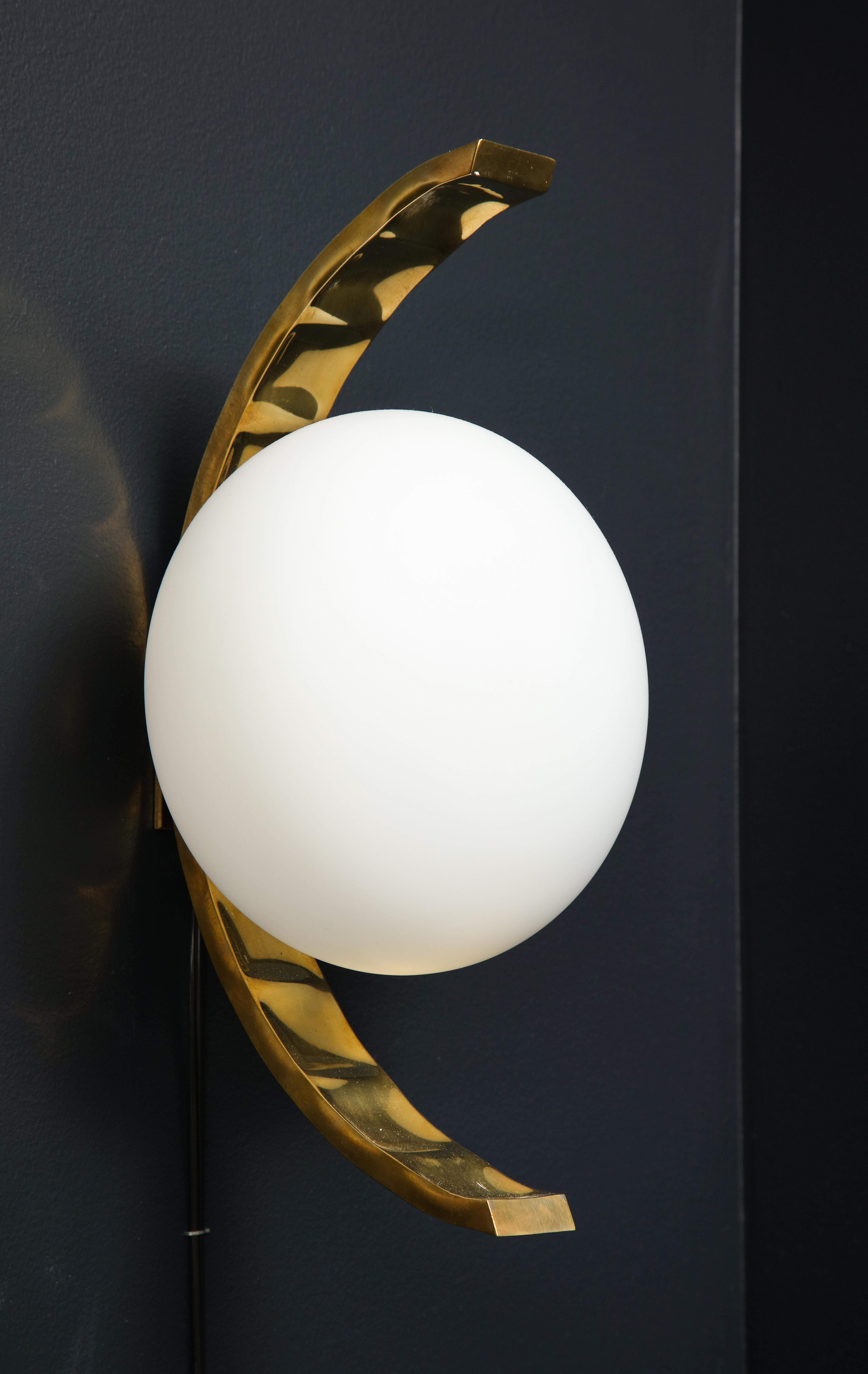 Pair of minimalist design white glass globe and brass sconces. A single large white glass globe is centered on top of a curved, arched stamped brass frame. Beautiful Italian design. Wired for U.S. standards. Each light holds a medium base bulb.