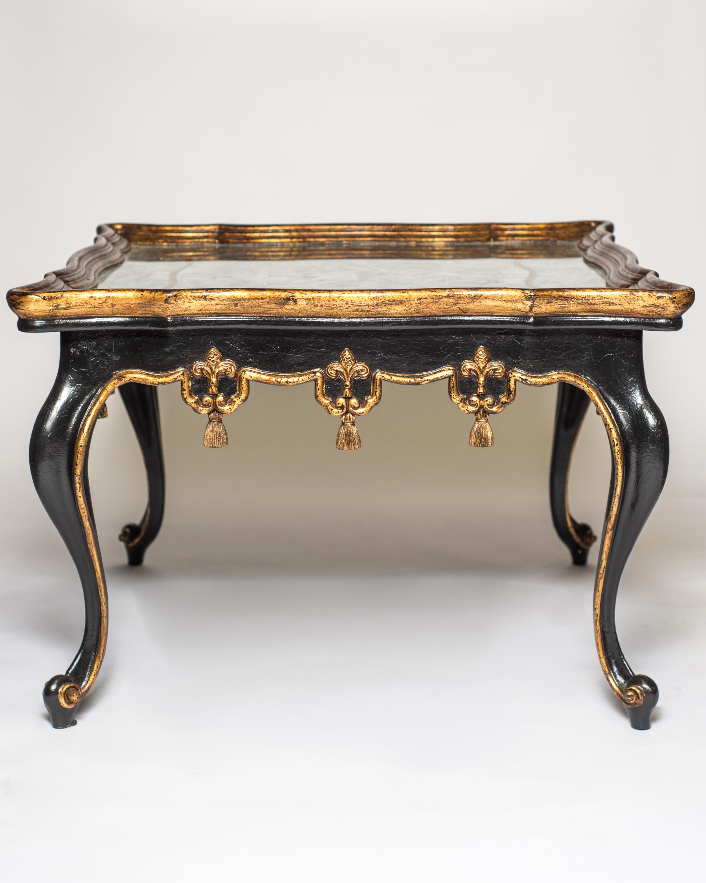 A pair of black and gilded carved wood tables with verse eglomise tops. Verre eglomise is a French term referring to the process of applying both a design and gilding onto the rear face of glass to produce a mirror finish. Carved scroll,