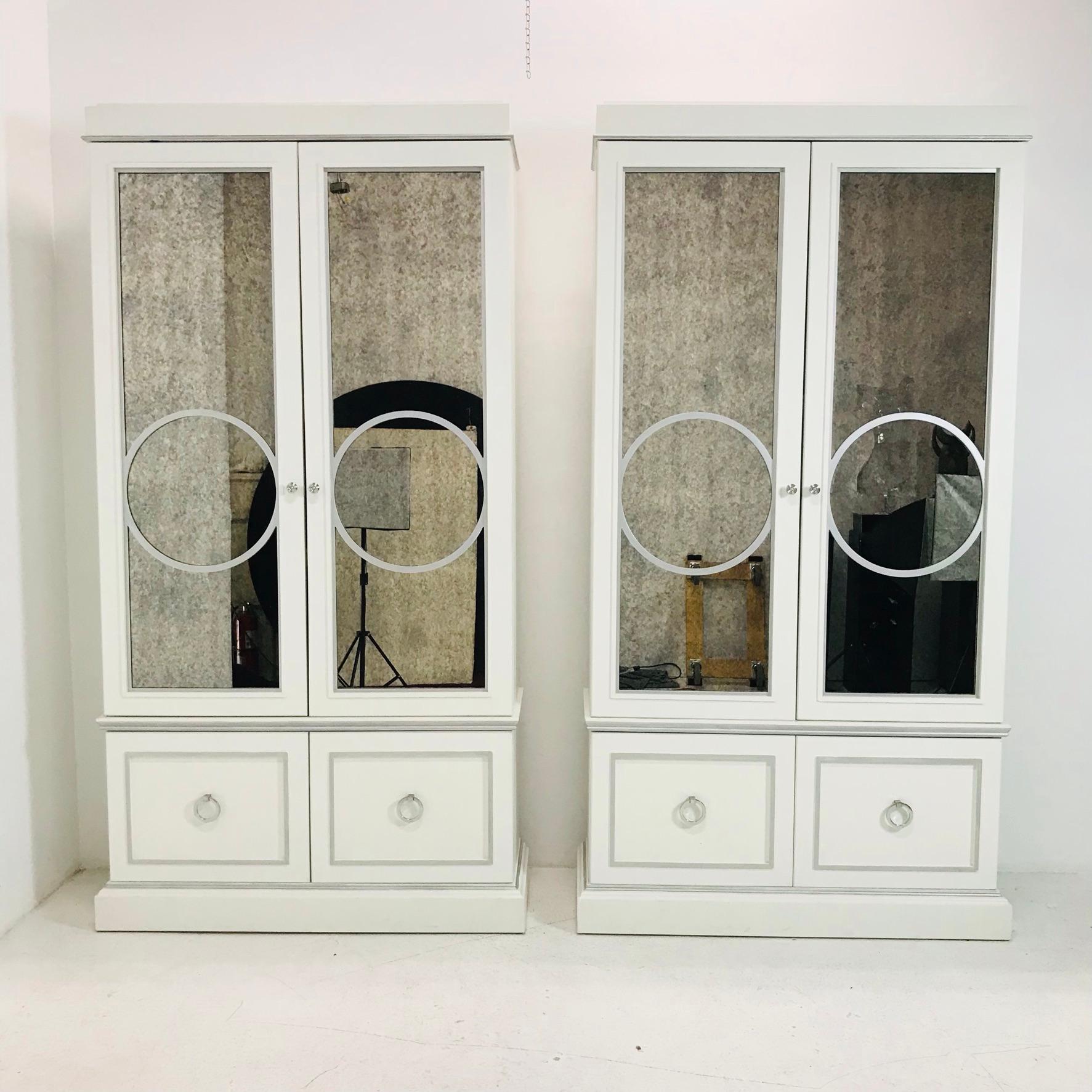 Sophisticated pair of white curio cabinets with antique mirror fronts. These glamorous cabinets feature double doors, interior shelves, and bottom storage drawers. Some minor cosmetic wear due to age and use but structurally very sound and in