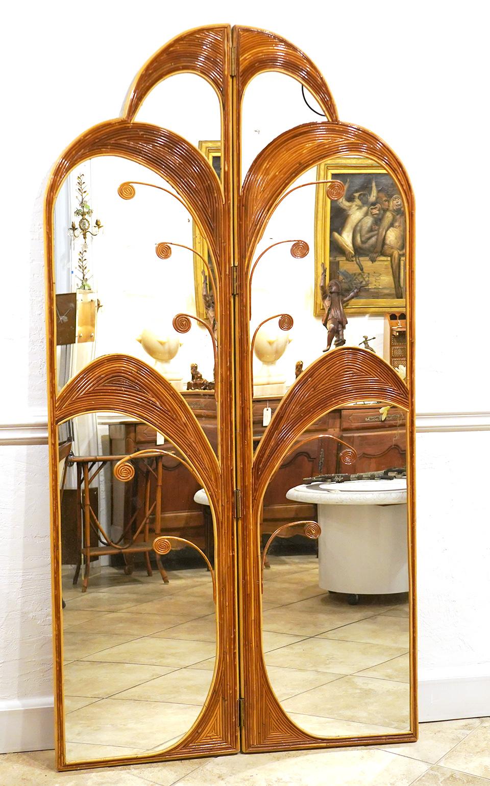 This pair of bamboo or rattan inlaid mirrored folding screens in the style of Vival del Sud feature art deco stylized palm trees hinged and with arched tops framing mirrors from top to bottom. The pair of panels can be used separately or as a