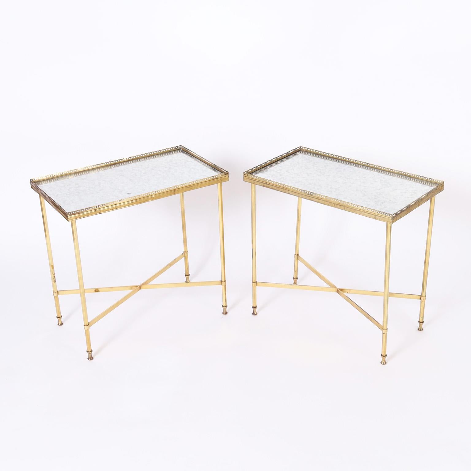 Chic pair of French stands with an unusual doré or gilt brass finish having distressed mirrored tops surrounded by perforated galleries. The bases have cross stretchers and elegant legs on hourglass feet.