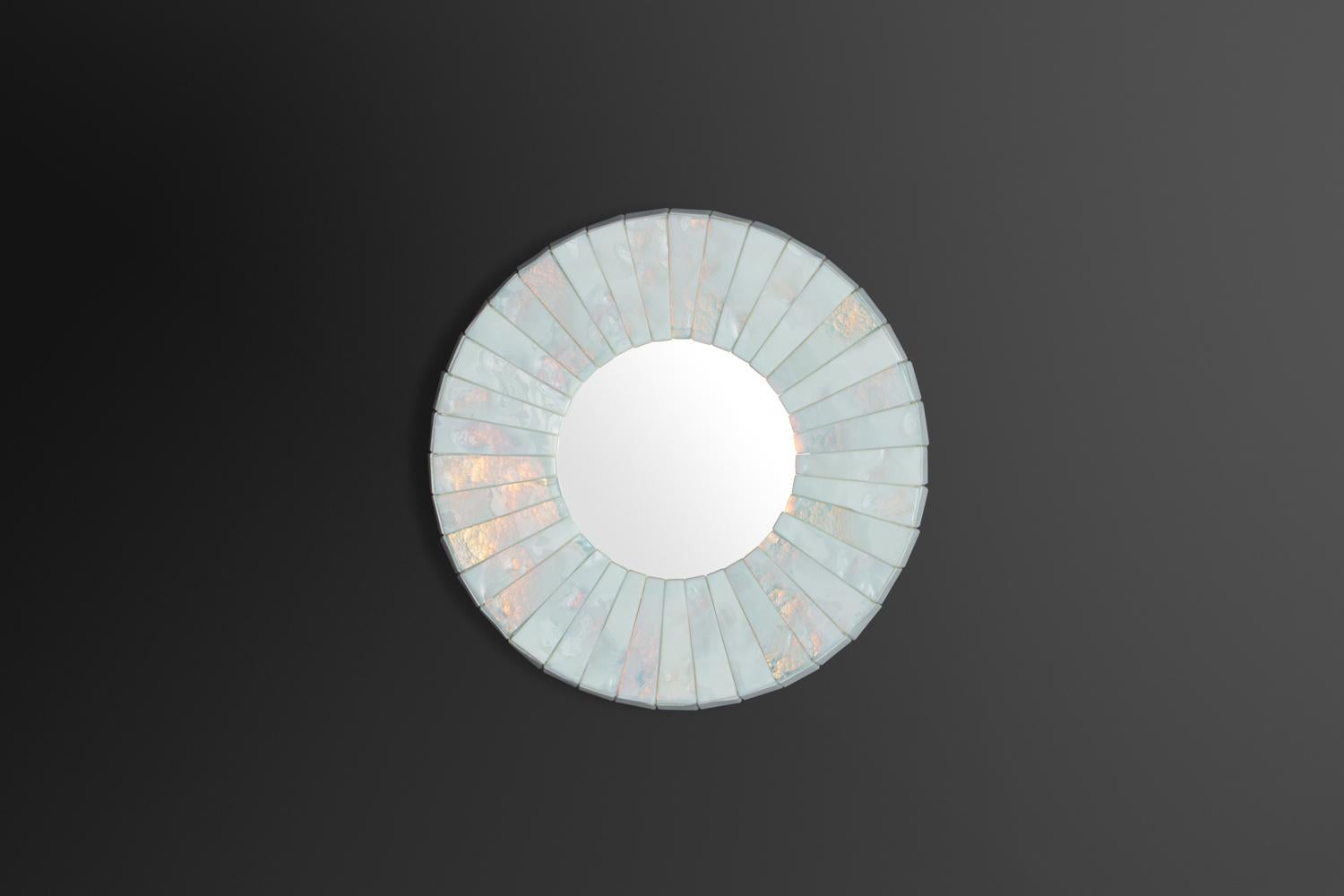 Hand-hewn wedges of thick, pitted milk glass with turquoise-rose iridescent tint, abutting similarly chiseled sides, encompassing a round mirrored glass plate.
Model “Leucos” mirror plate diameter 17.5.