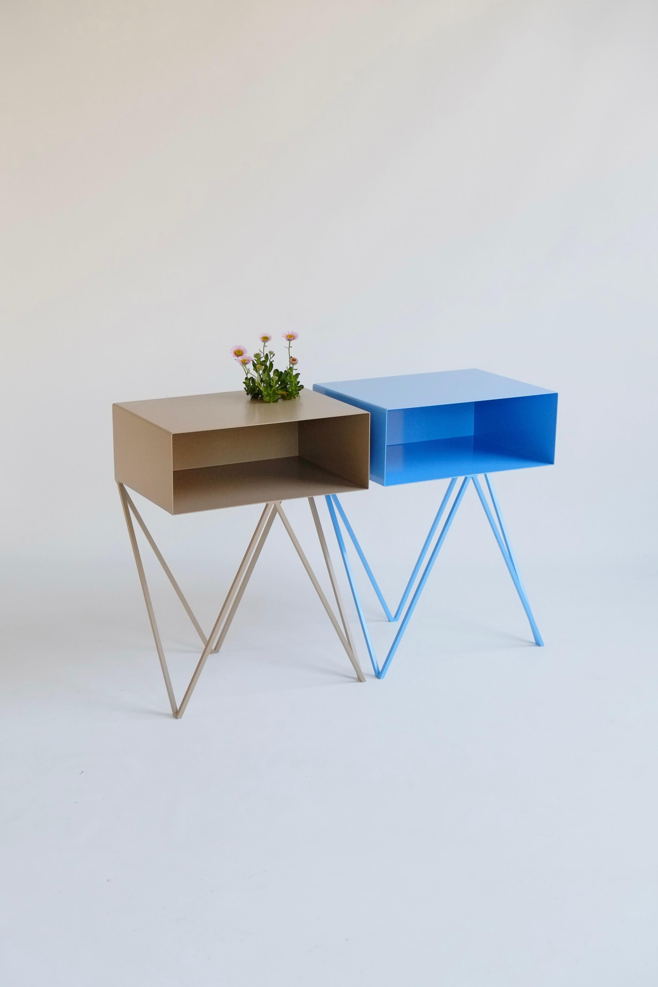 A beautiful pair of mismatched ice blue and coco Robot bedside tables. The Robot side table features an open shelf on zig zag legs. A fun and functional design made of solid steel, one is powder-coated in ice blue and the other in coco. The clean