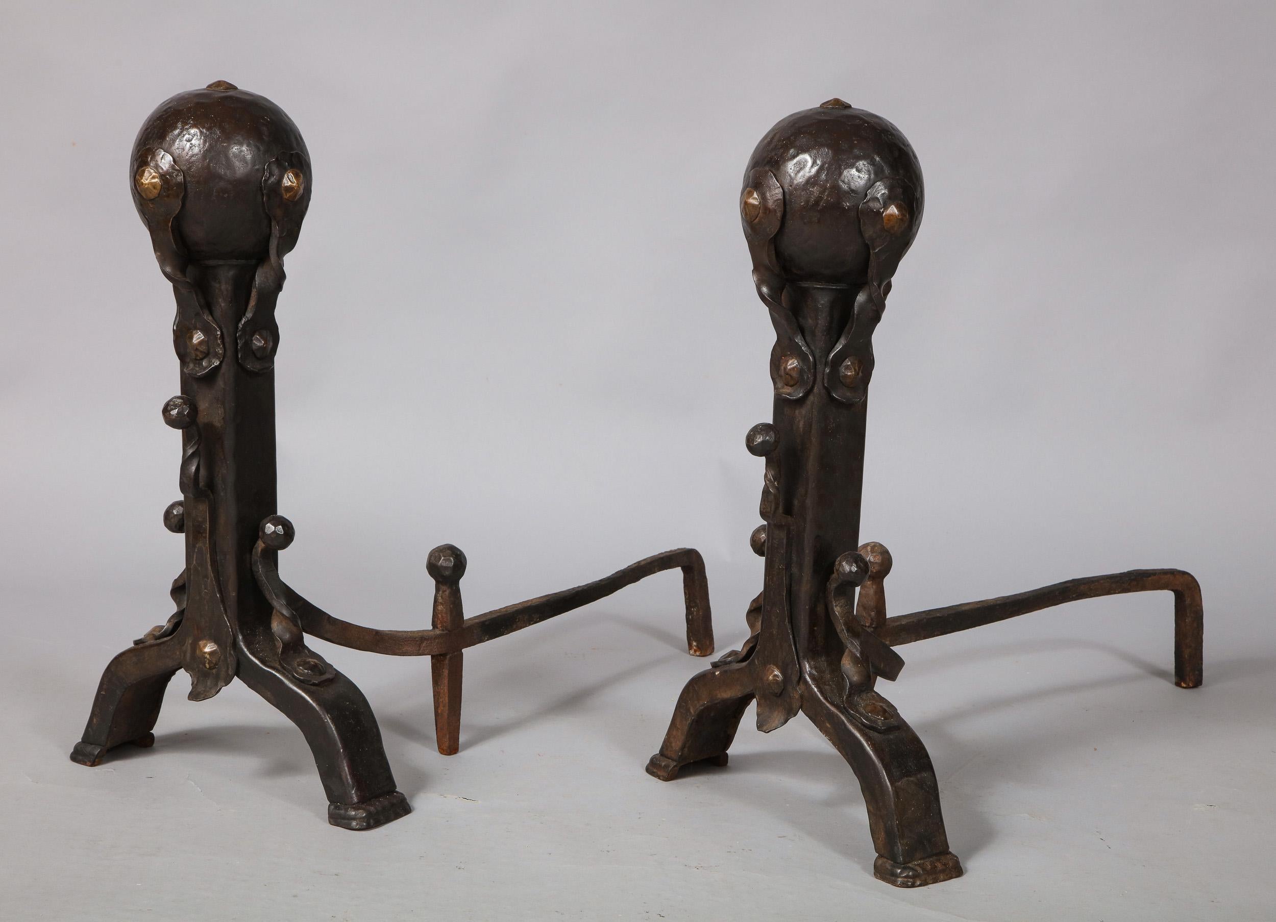 Fine pair of Arts & Crafts period patinated iron and bronze andirons, having two hammered sphere finials mounted with strapwork twists with beaten bronze rivets over similarly mounted shafts and standing on arched feet.