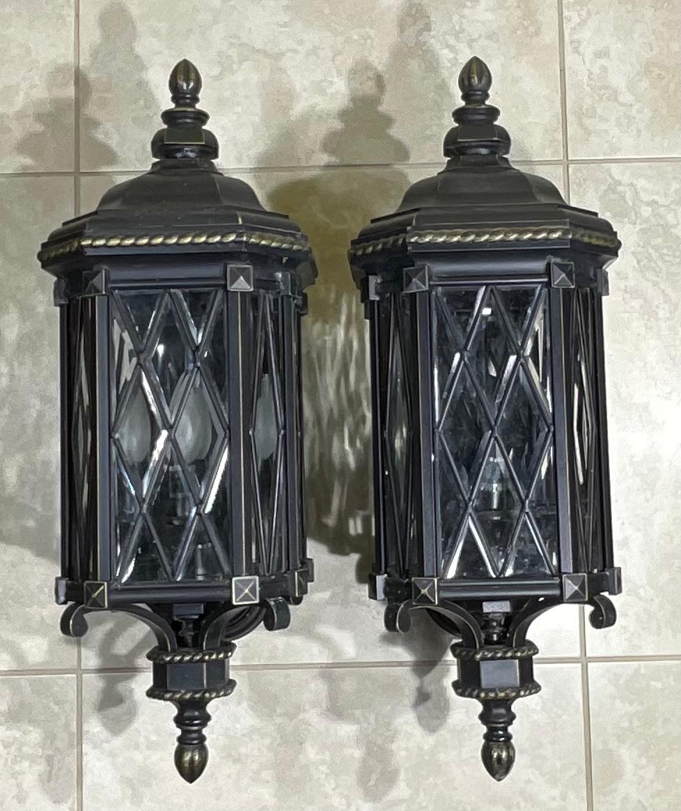 The Great Outdoors light brings class and sophistication to the space with this antique Mizner style wall sconce. Its Black finish with gold , The elegant work of the sand-cast aluminum continuous cage contrasts with the clear beveled glass inside.