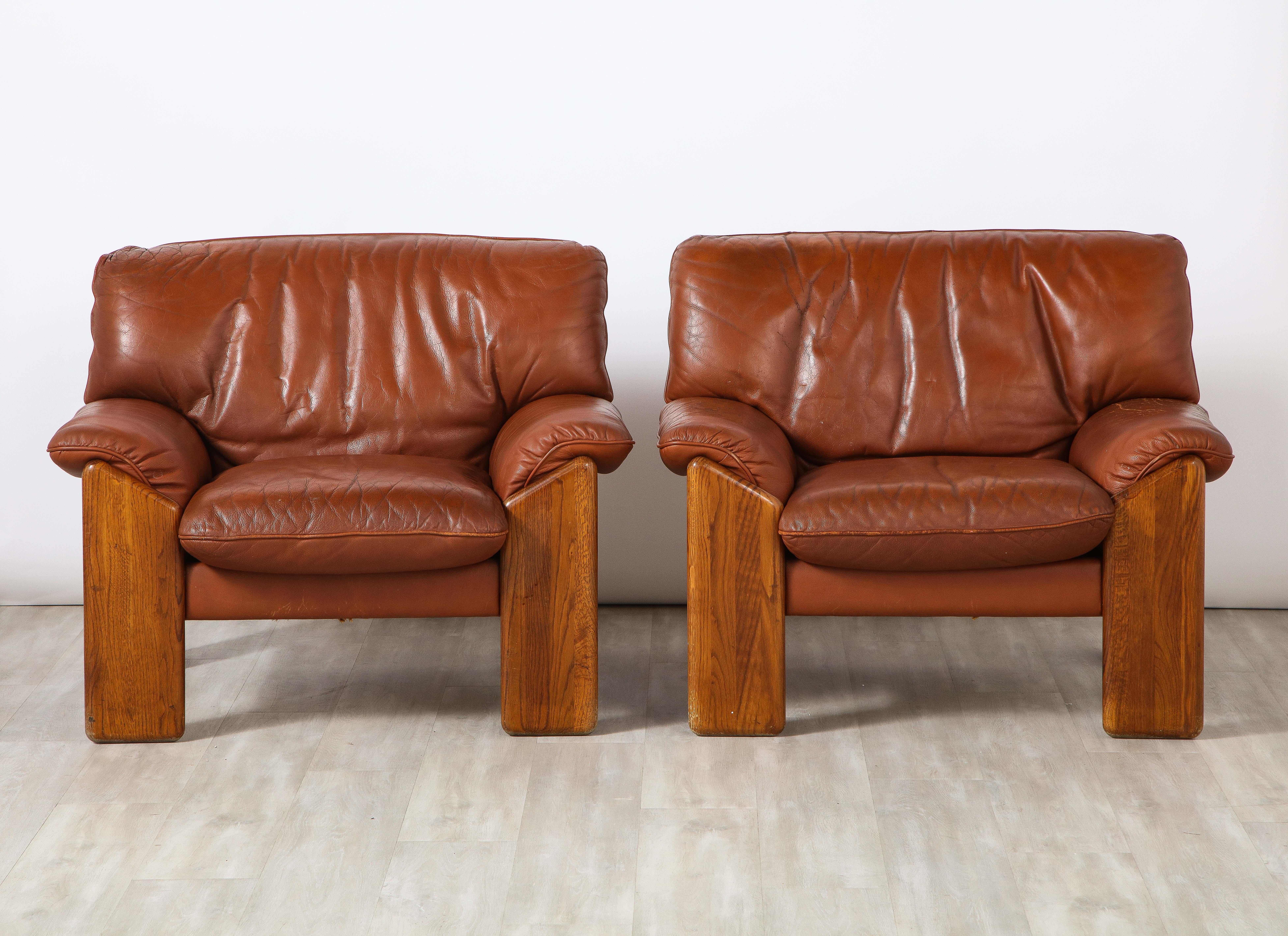 A pair of walnut and leather lounge chairs by Mobil Girgi, made in the 1970's, Italy. Stamped. Beautifully designed with angled front legs which extend to the sides and back of the chairs, the back support is slightly curved. The flat upholstered