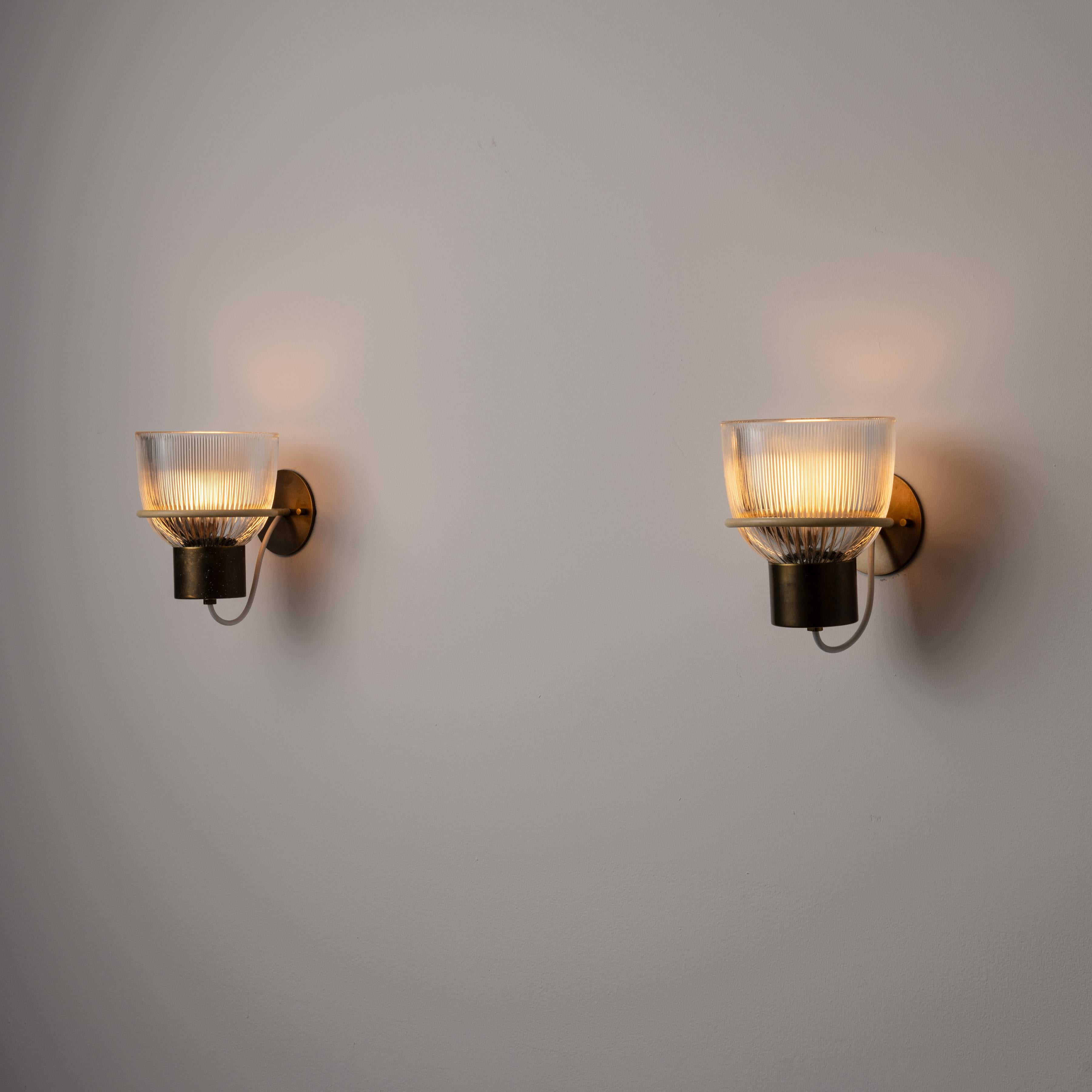 Pair of Model 1112 Sconces by Tito Agnoli for Oluce. Designed and manufactured in Italy, in 1959. Bell shaped sconces with brass frame and detailing and custom reeded glass diffusers. The sconces are held upright by an enameled hoop that is adhered
