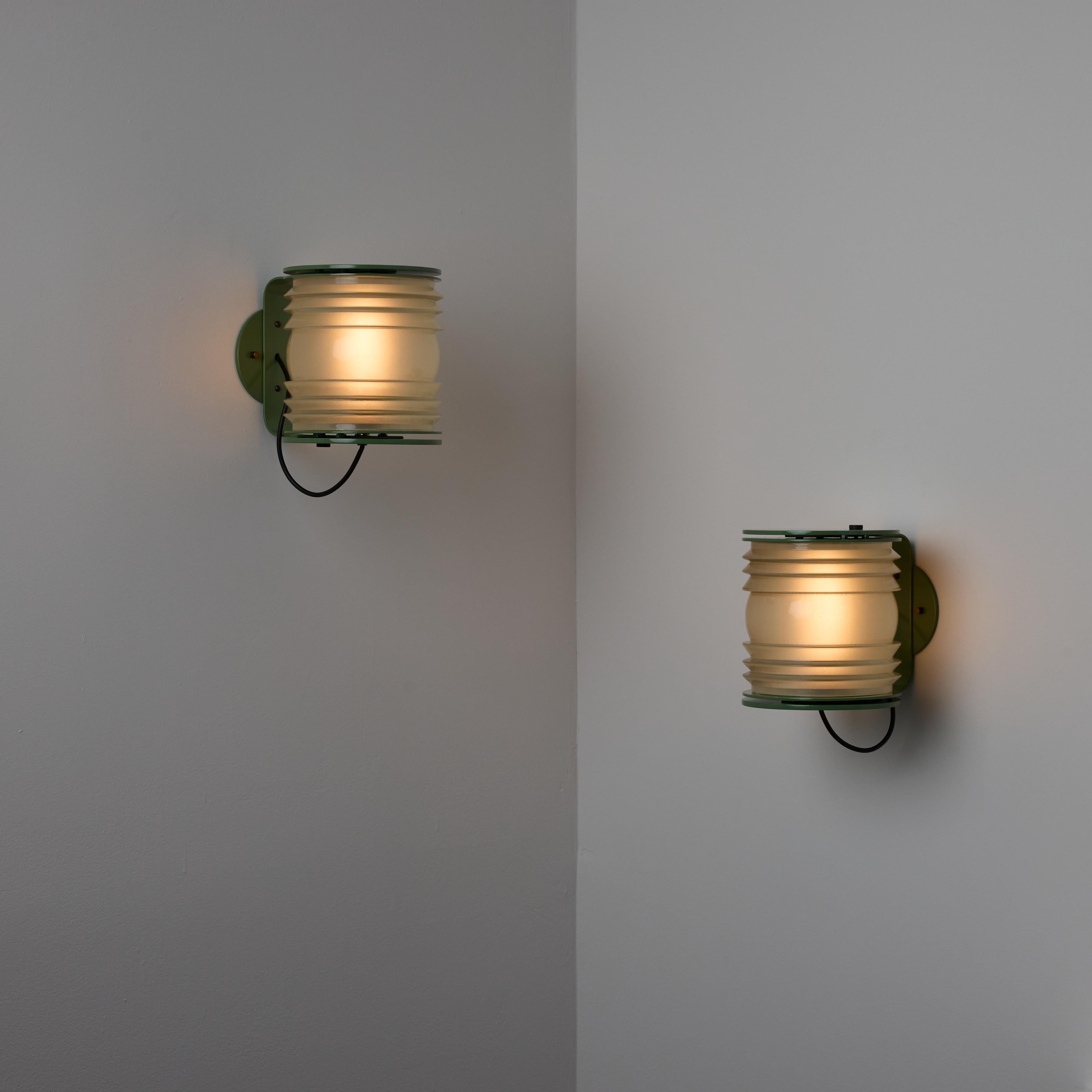 Pareja de apliques Modelo 1151 de Joe Colombo para Oluce. Diseñado y fabricado en Italia hacia 1965. El grueso cristal moldeado se aloja entre un soporte en forma de hickey de color verde salvia con recubrimiento en polvo. Detalles de remates de