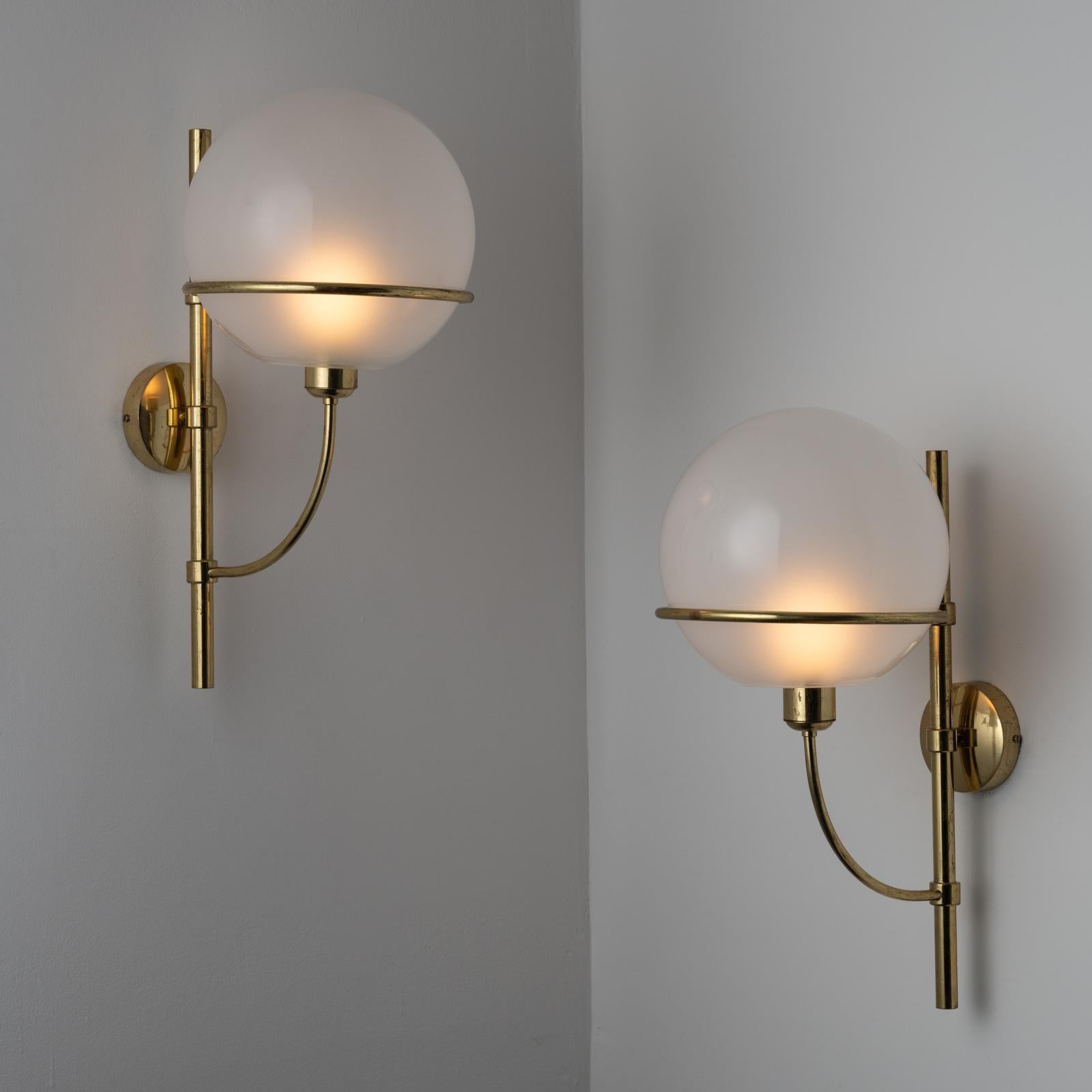 Model 160 'Lyndon' Sconces by Vico Magistretti for Oluce. Designed and manufactured in Italy, circa the 1970s. Polished brass armatures which are vertically adjustable hold an etched glass globe. Each sconce holds one E27 socket type, adapted for