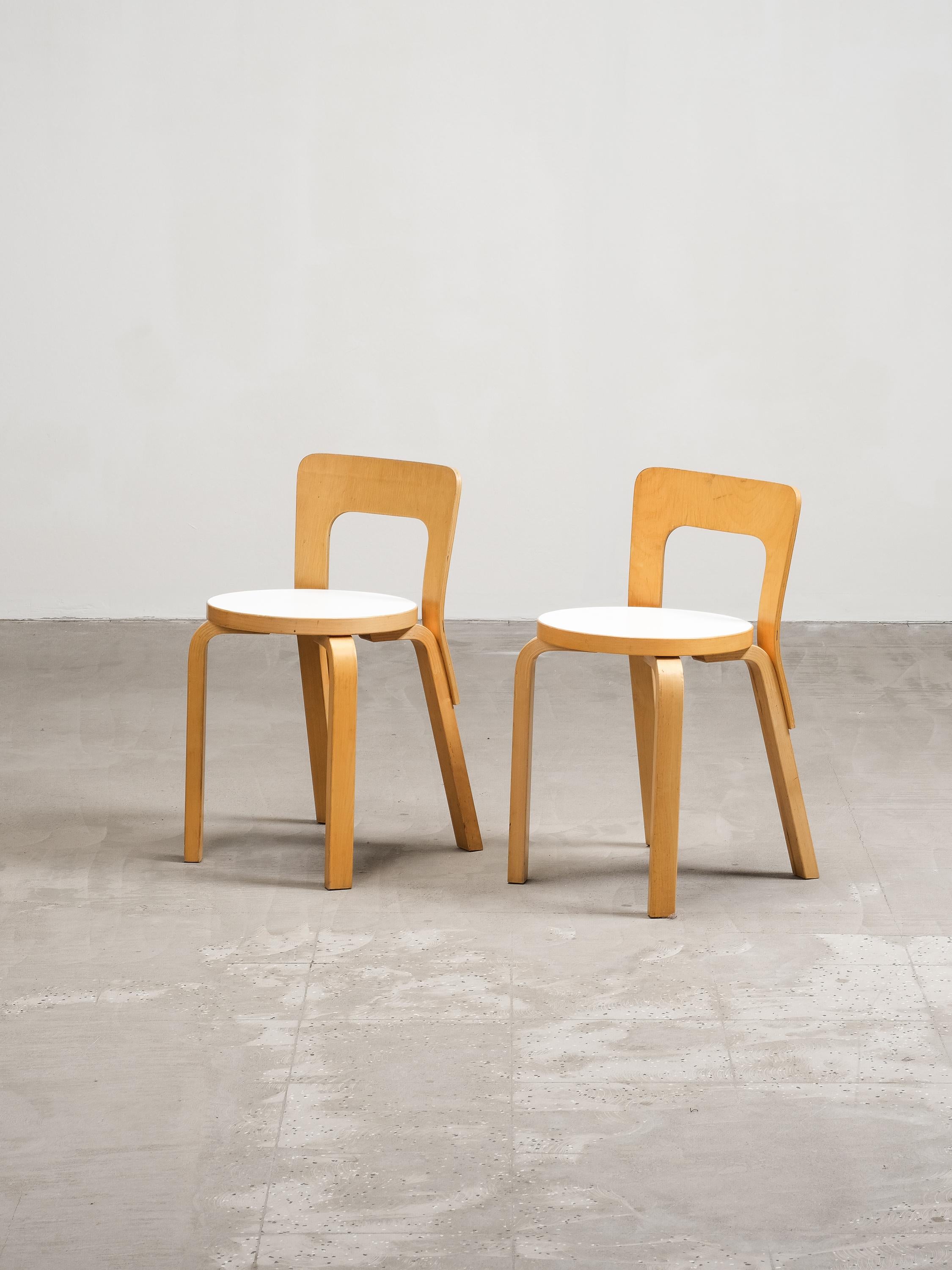 Una coppia di sedie Model 65 senza tempo, disegnate dal leggendario Alvar Aalto per Artek nel 1935. Queste sedie iconiche mostrano l'approccio rivoluzionario di Aalto+Aalto al design dei mobili, caratterizzato da forme semplici e organiche e