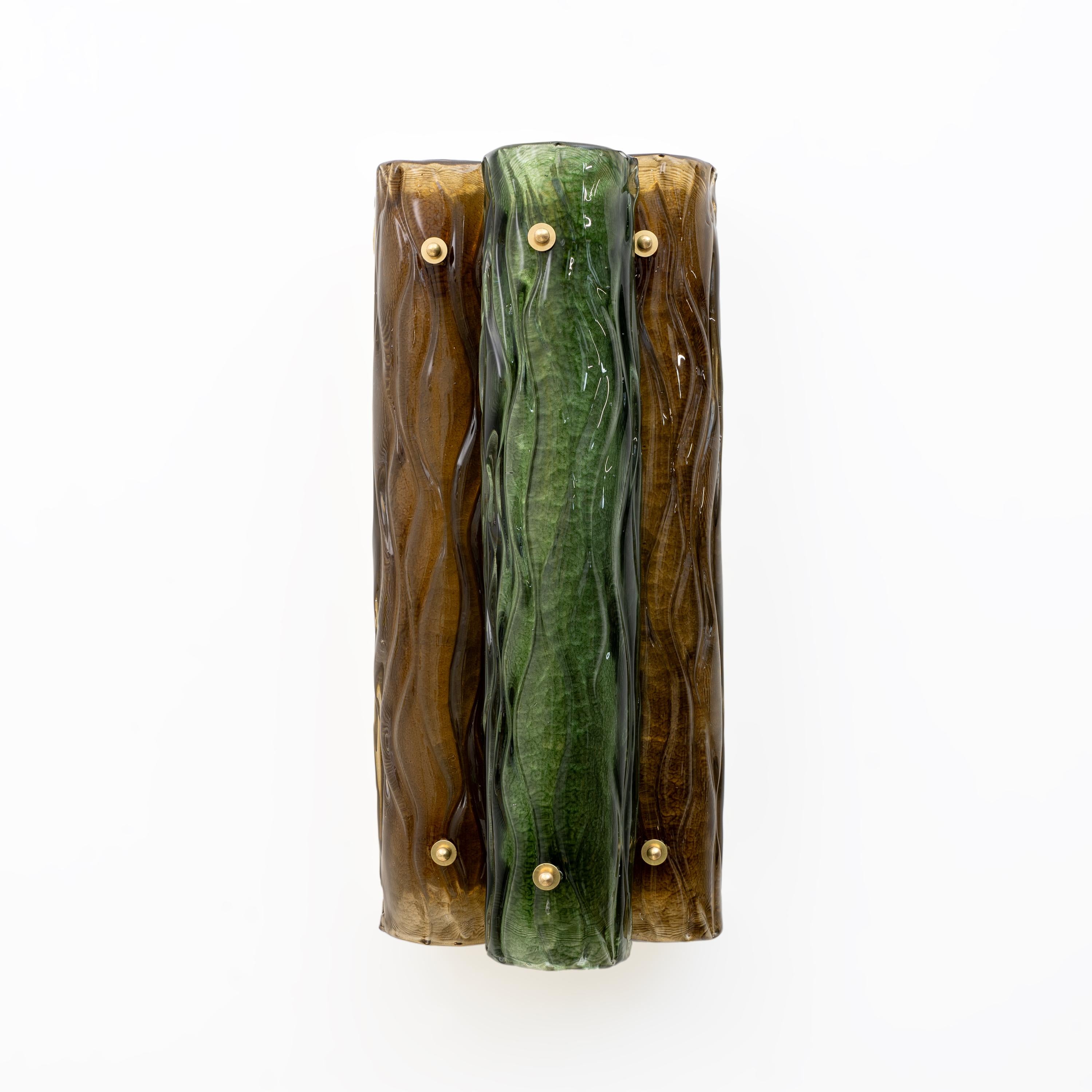 Coppia di lampade in vetro di Murano, composte da tre forme cilindriche verticali raggruppate. I cilindri hanno una superficie ondulata e strutturata che crea un design organico e fluido. Uno dei cilindri è verde, mentre gli altri due sono di colore