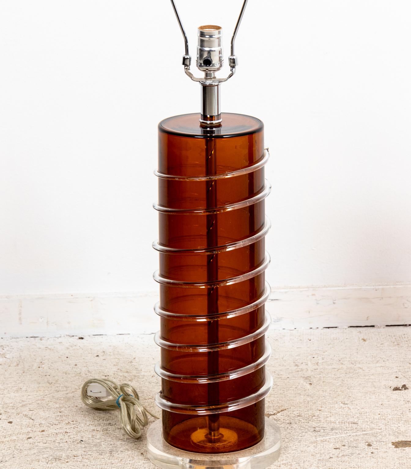 Circa 1990s-2000s pair of Modern style Amber glass table lamps. The lamps feature a glass body wrapped with corkscrew shaped accent glass on a Lucite base. Rewired. The piece measures 23.00 Inches to the top of the socket. Please note of wear