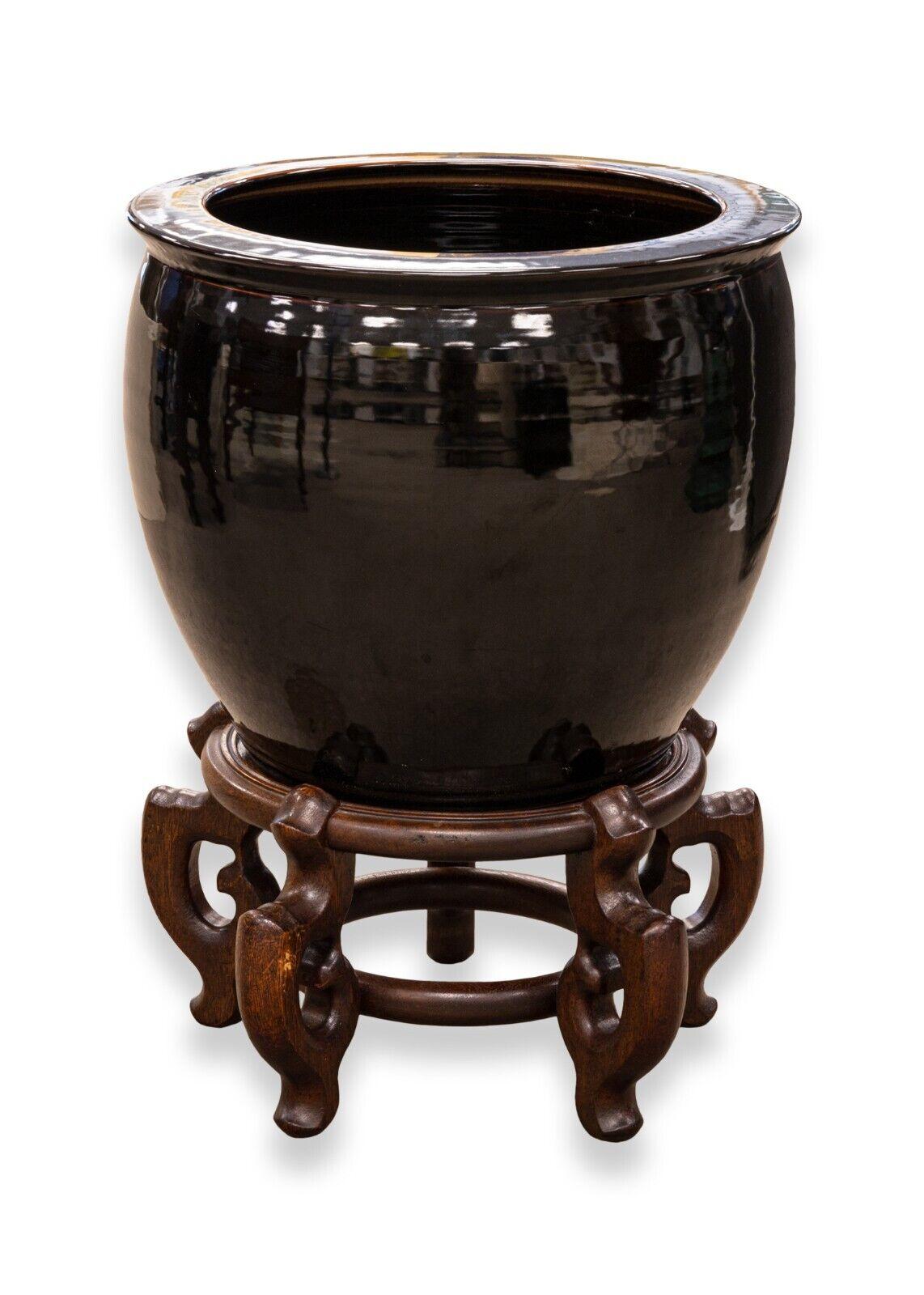 A timeless pair of Asian urn floor ceramic vases on ornate wooden stands. These vases have a rich black colored glaze with hints of color around the rim. They sit on a pair of stunning ornate wooden stands. These floor vases would look even more