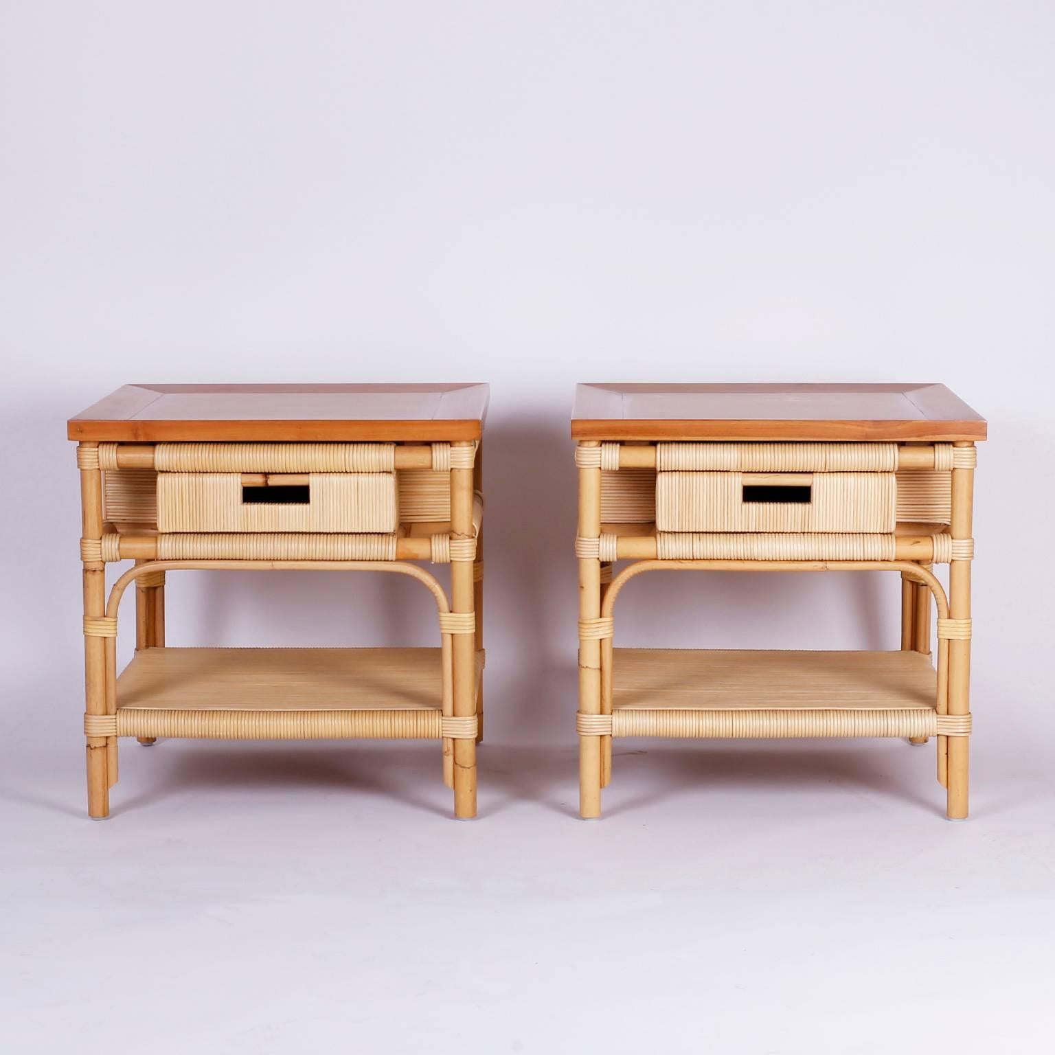 Dashing pair of one drawer end tables or nightstands with a handy lower plateau, cross banded poplar tops, and a bamboo frame wrapped with reed. Highest quality and unsurpassed casual elegance. John Hutton for Donghia, Merbau collection. Signed