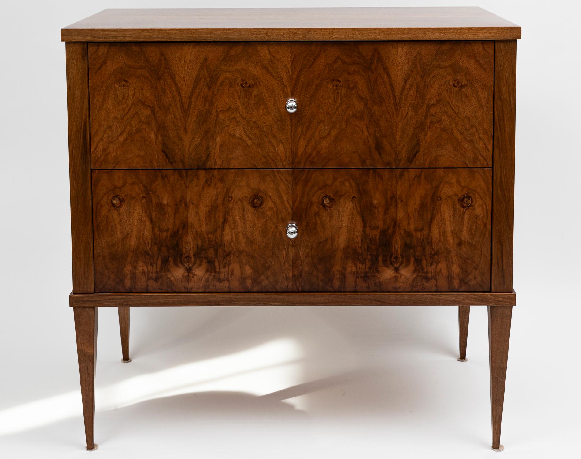 A newly handmade pair of sleek Modern Biedermeier chests made of solid walnut wood and comprised of two deep drawers on high tapered and straight legs. Wood is finished in a matte low luster finish.   Polished nickel on brass pulls open each drawer
