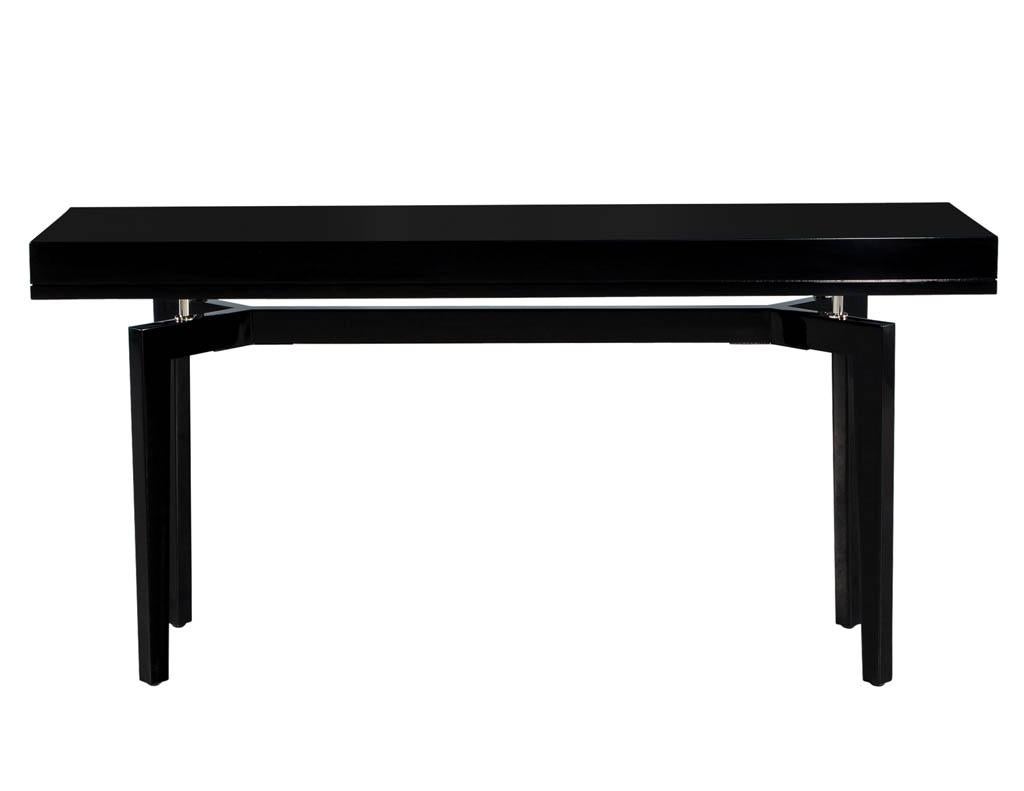 Pair of Modern Black Lacquered Console Tables. America, circa 1970s. Masterfully restored in a high gloss black lacquered finish. Unique 1970s Mid-Century Modern design with stretcher base and beautiful stainless-steel accent supports. Price