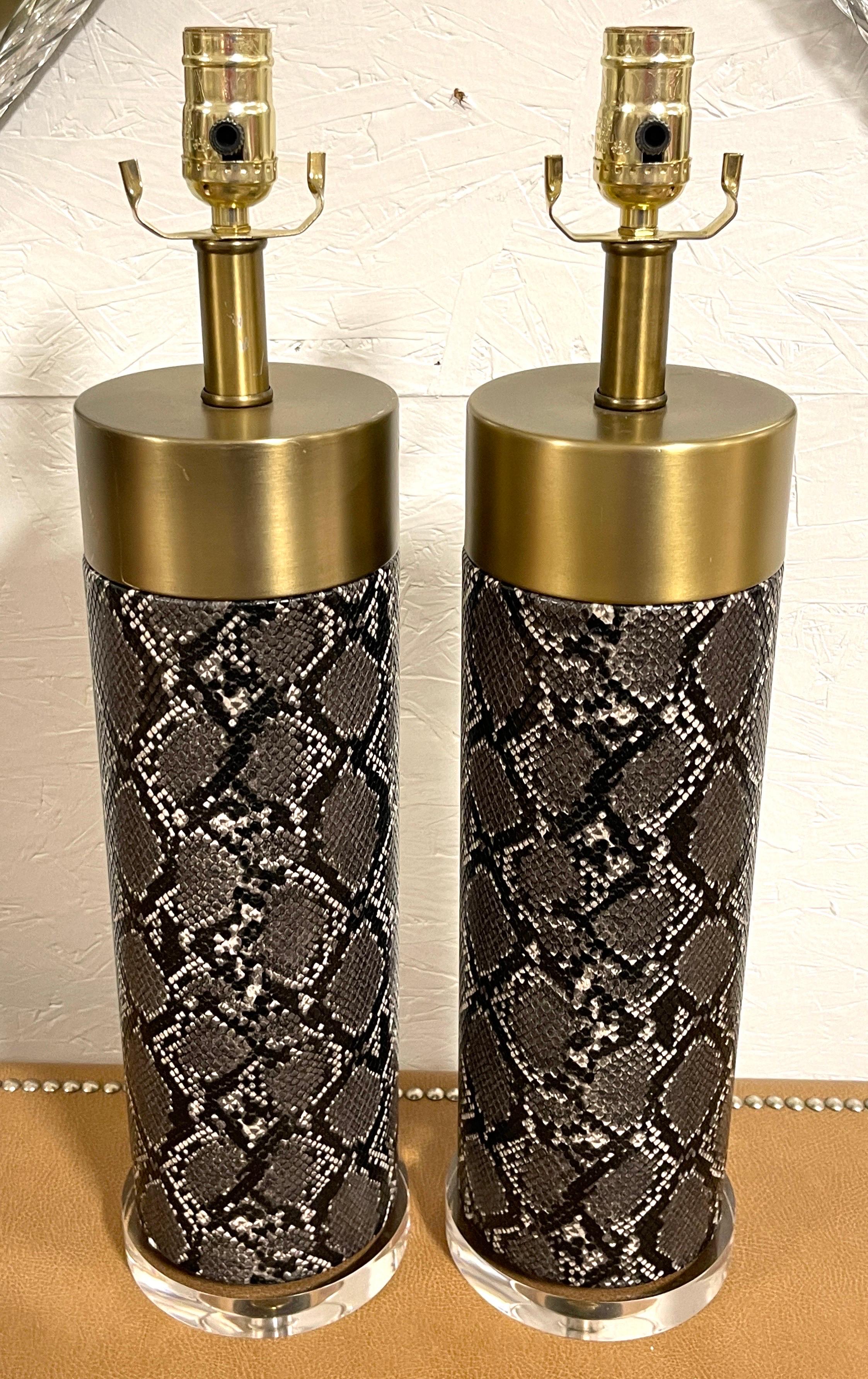 Pair of Modern brass, faux snakeskin & lucite column lamps.
Circa 1990s.

Each one with a large satin brass cap, with a cylindrical column with applied realistic, book-matched embossed and polychromed black and white leather 'snakeskin' raised on