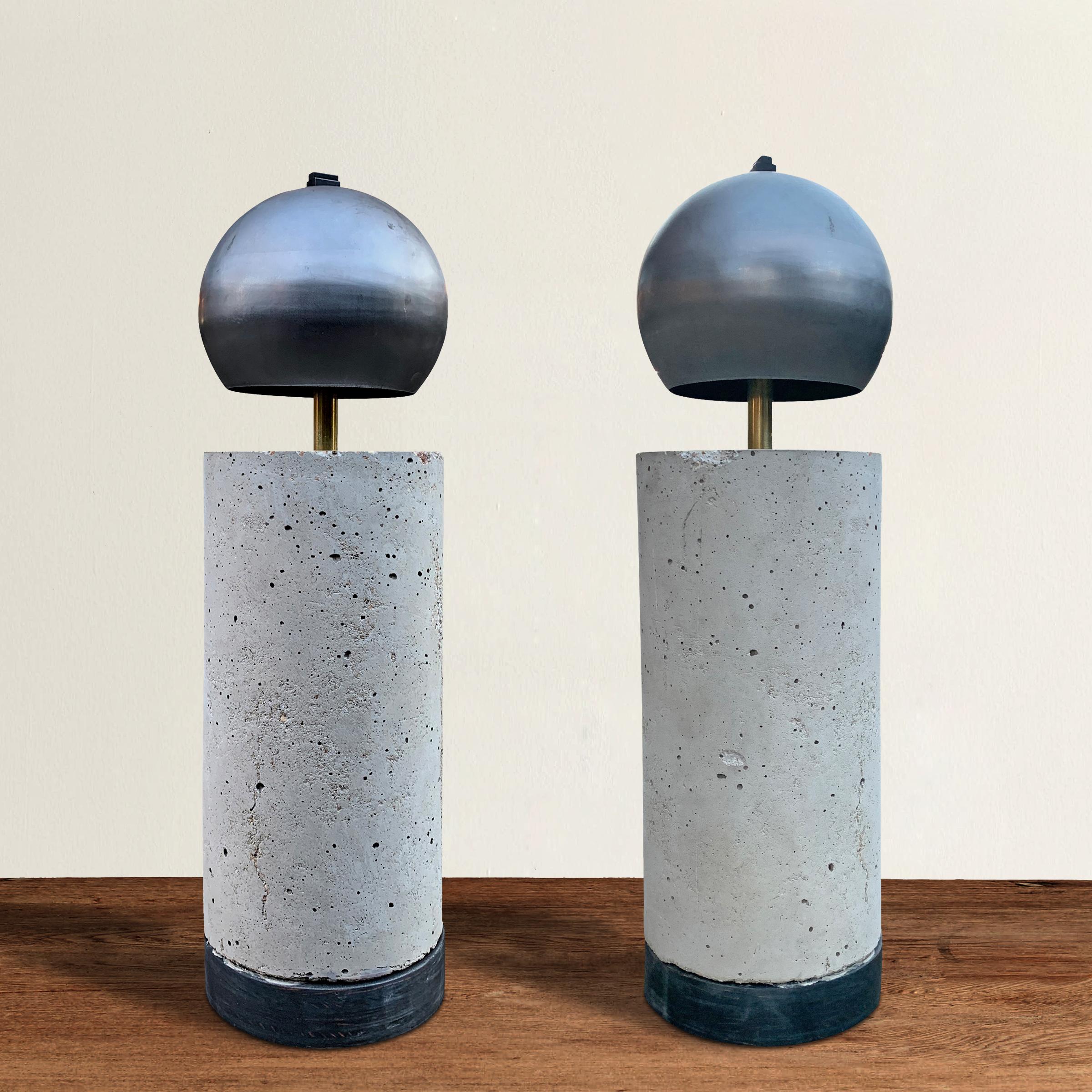 A sharp pair of contemporary American artist-made table lamps designed with a Brutalist spirit, and constructed with steel dome shades, cylindrical cement bodies, with wood bases. Electrified for US with two LED bulbs each.
