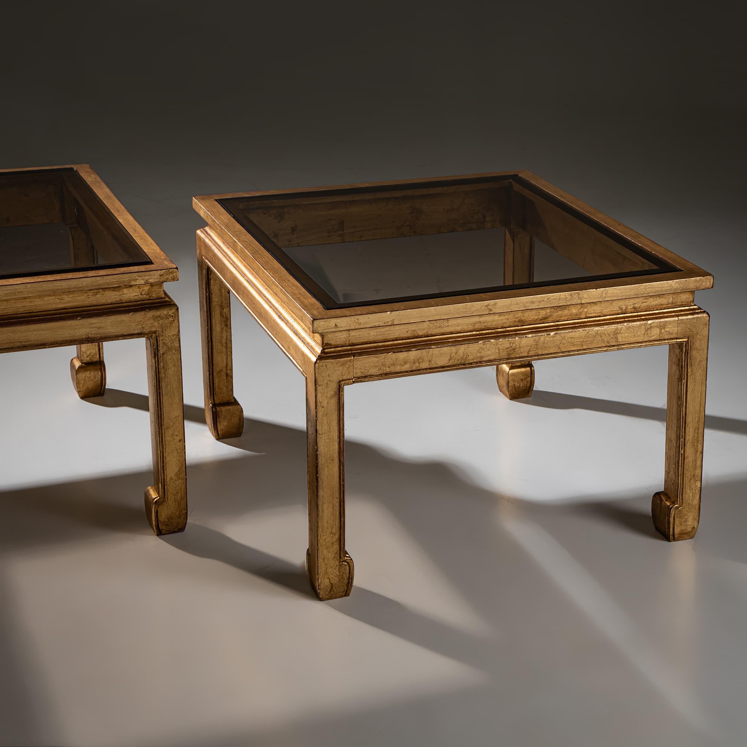 Paire de tables basses carrées modernes avec cadres dorés et plateaux en verre. Les pieds subtilement évasés avec des pieds courbés reflètent des éléments de design inspirés de l'esthétique asiatique.