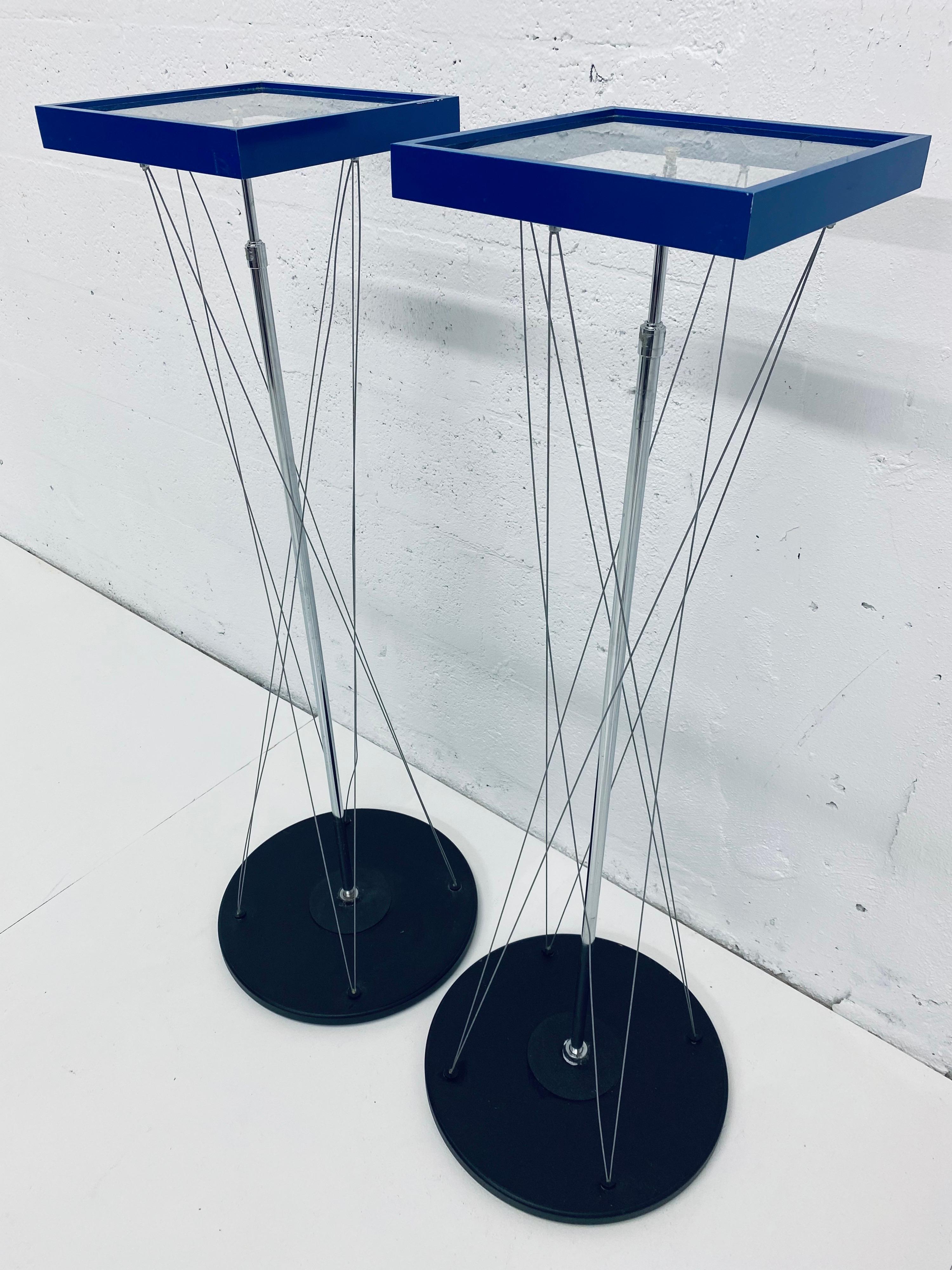 Two contemporary pedestal tables with electric blue steel frame top with glass insert on a steel shaft and held in place by tension wires connected to a black base.

Top overall dimensions:
W 10.25