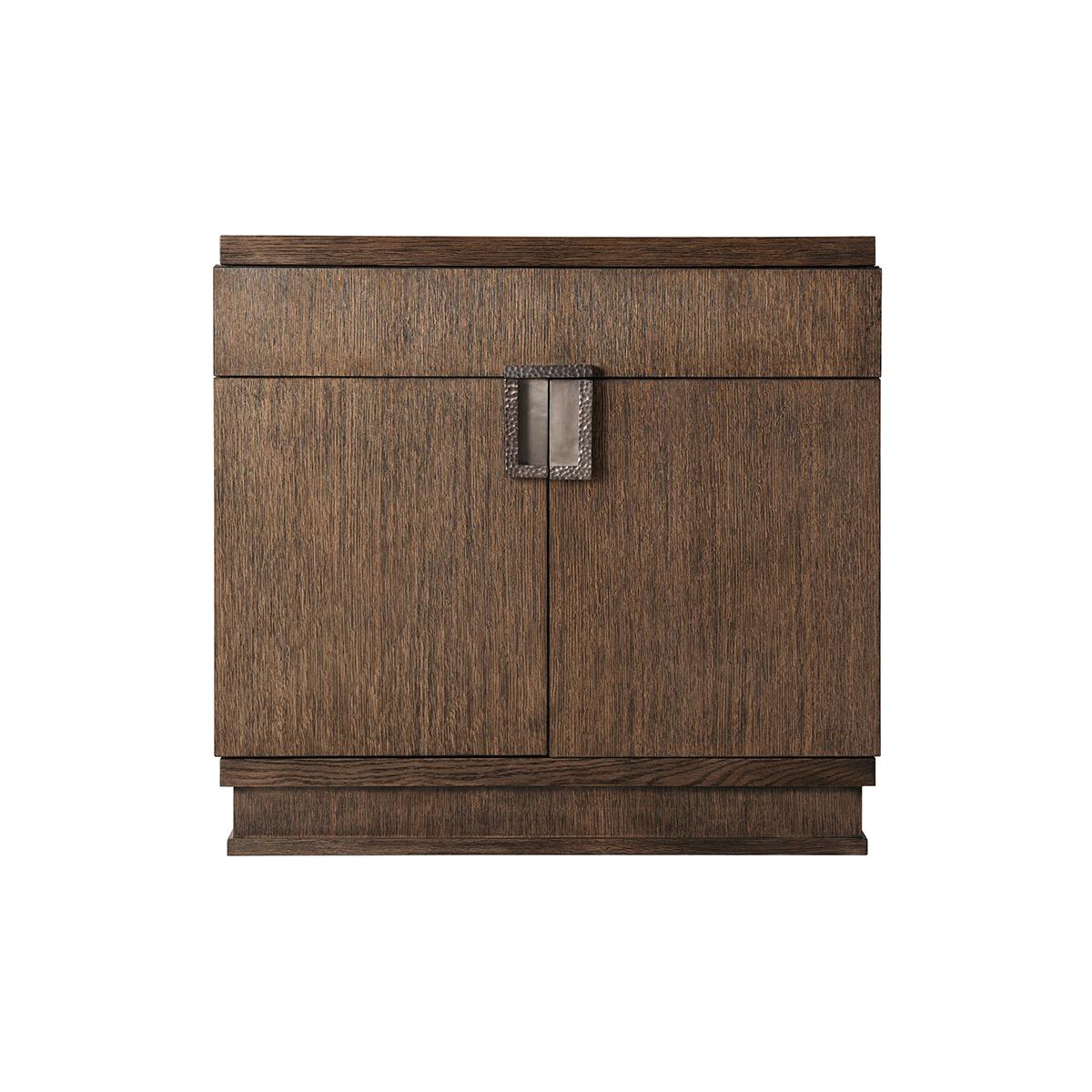 With a quartered oak veneer in the Charteris finish. With a rectangular top above a frieze drawer and two cabinet doors. With a modern brass finish handle with a hammered design. 
Dimensions: 30